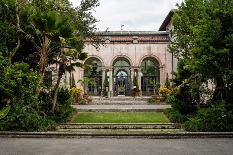 A stately building with arched entrances, surrounded by lush greenery and trees. The architecture is reminiscent of historical or government buildings.