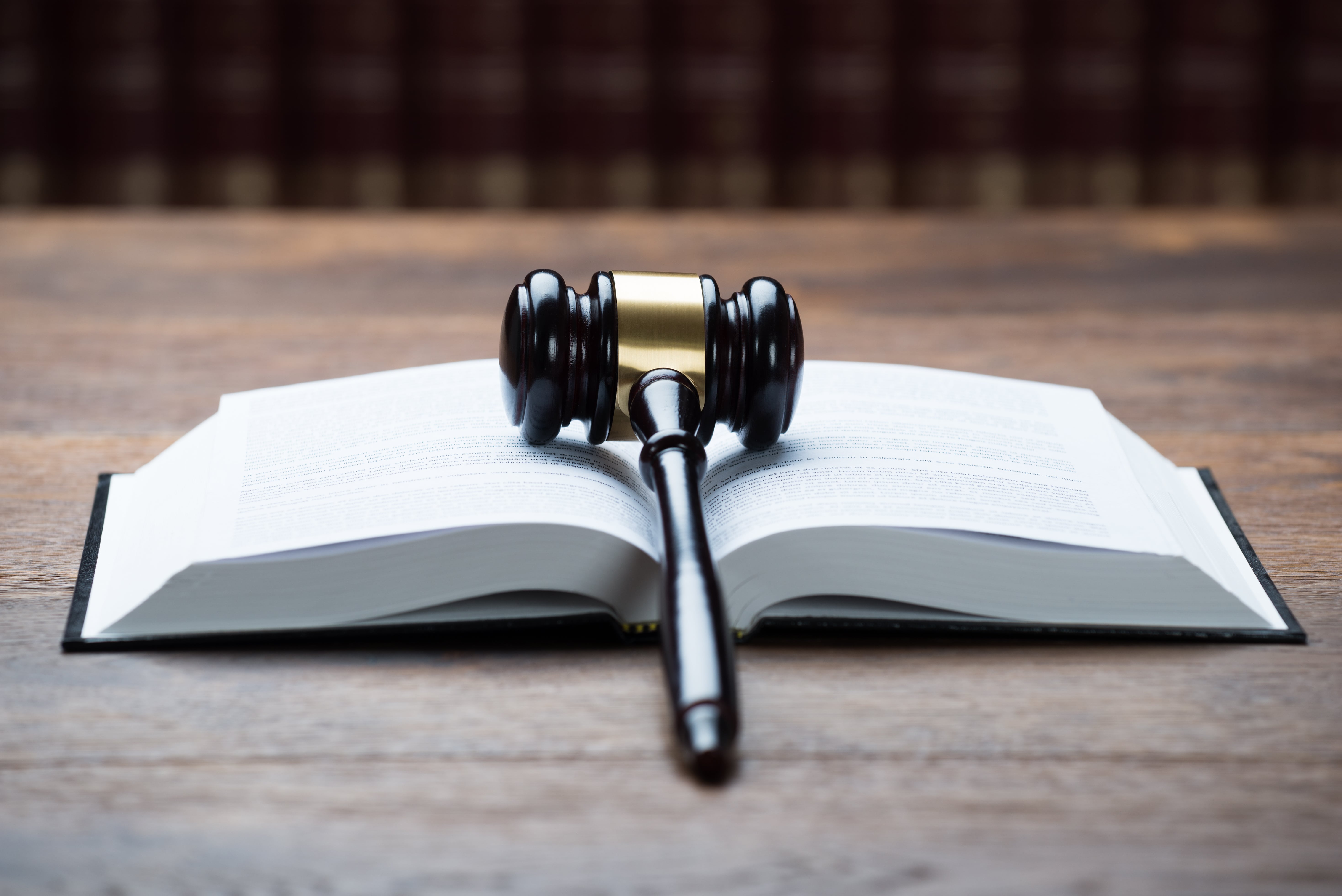 A wooden judge’s gavel resting on an open law book, symbolizing legal decisions, regulations, and justice. The background features a row of blurred legal books.