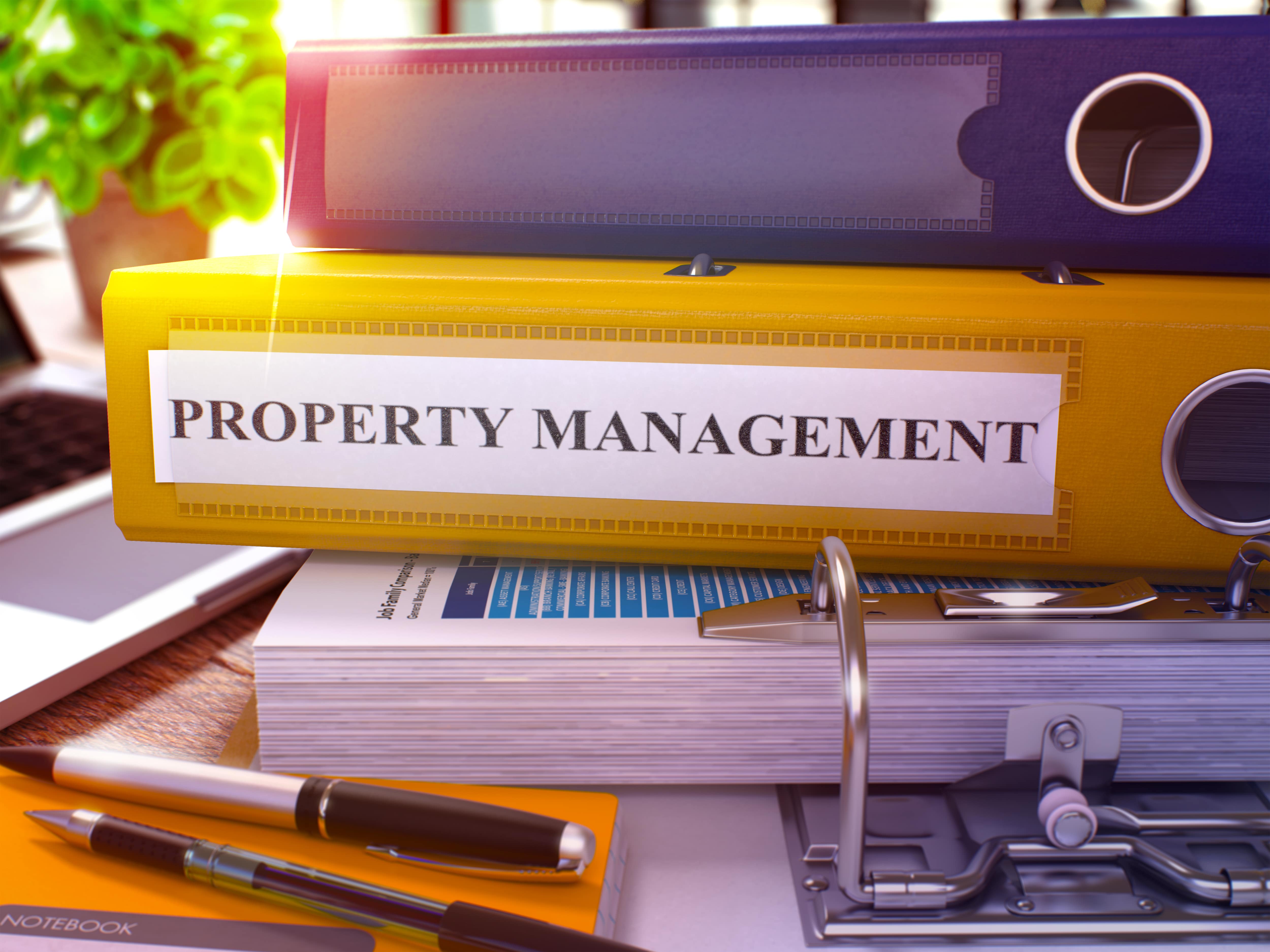 A close-up of colorful binders labeled 'Property Management' on a desk with paperwork, pens, and a notebook, symbolizing organization, real estate management, and professional services.