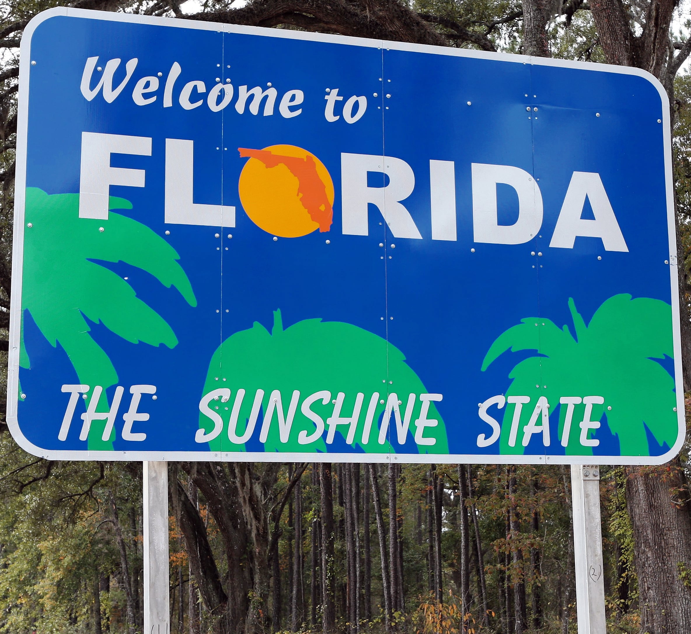 Bright blue ‘Welcome to Florida’ sign with palm trees and the phrase ‘The Sunshine State.