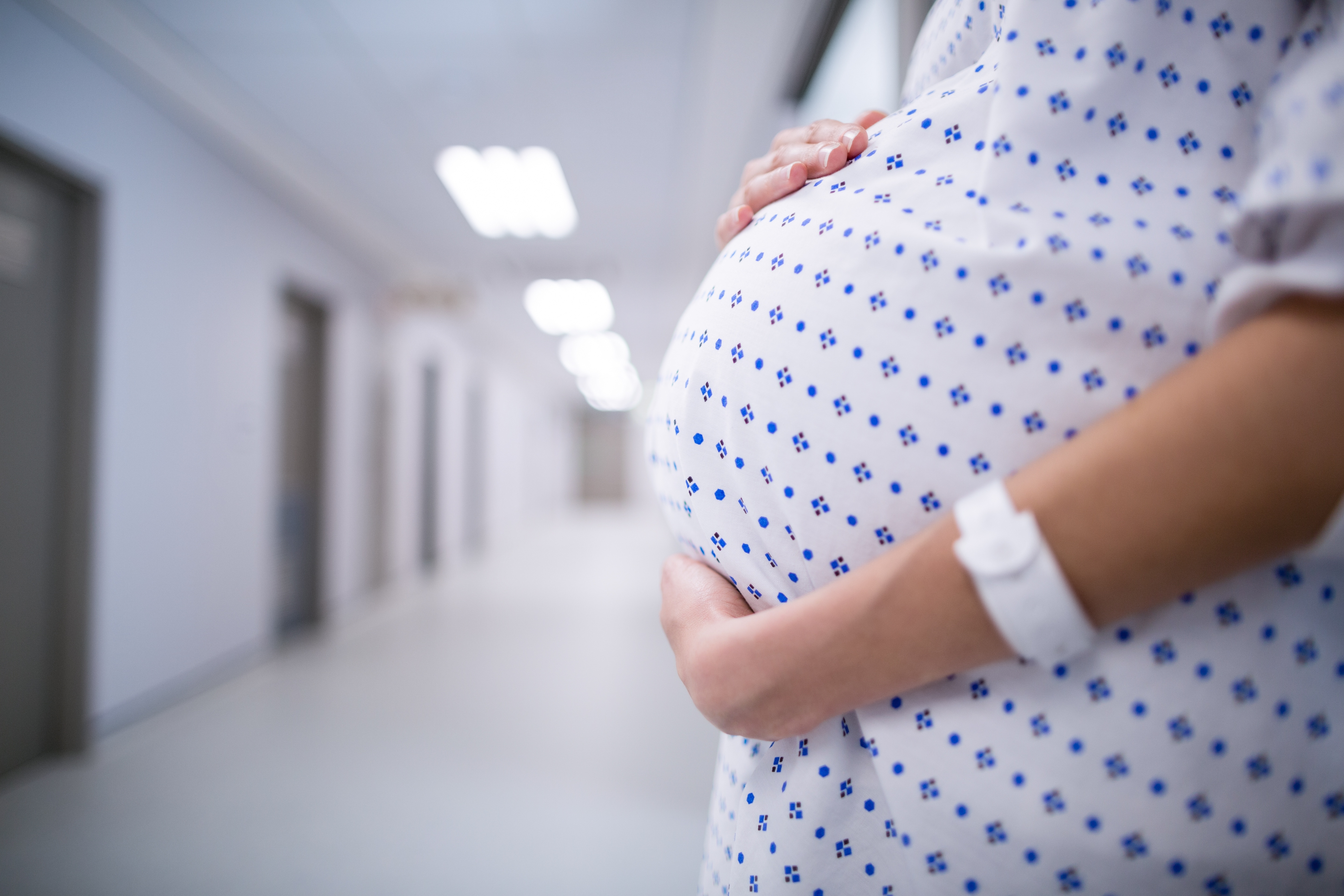 Pregnant woman in hospital gown cradling her belly.