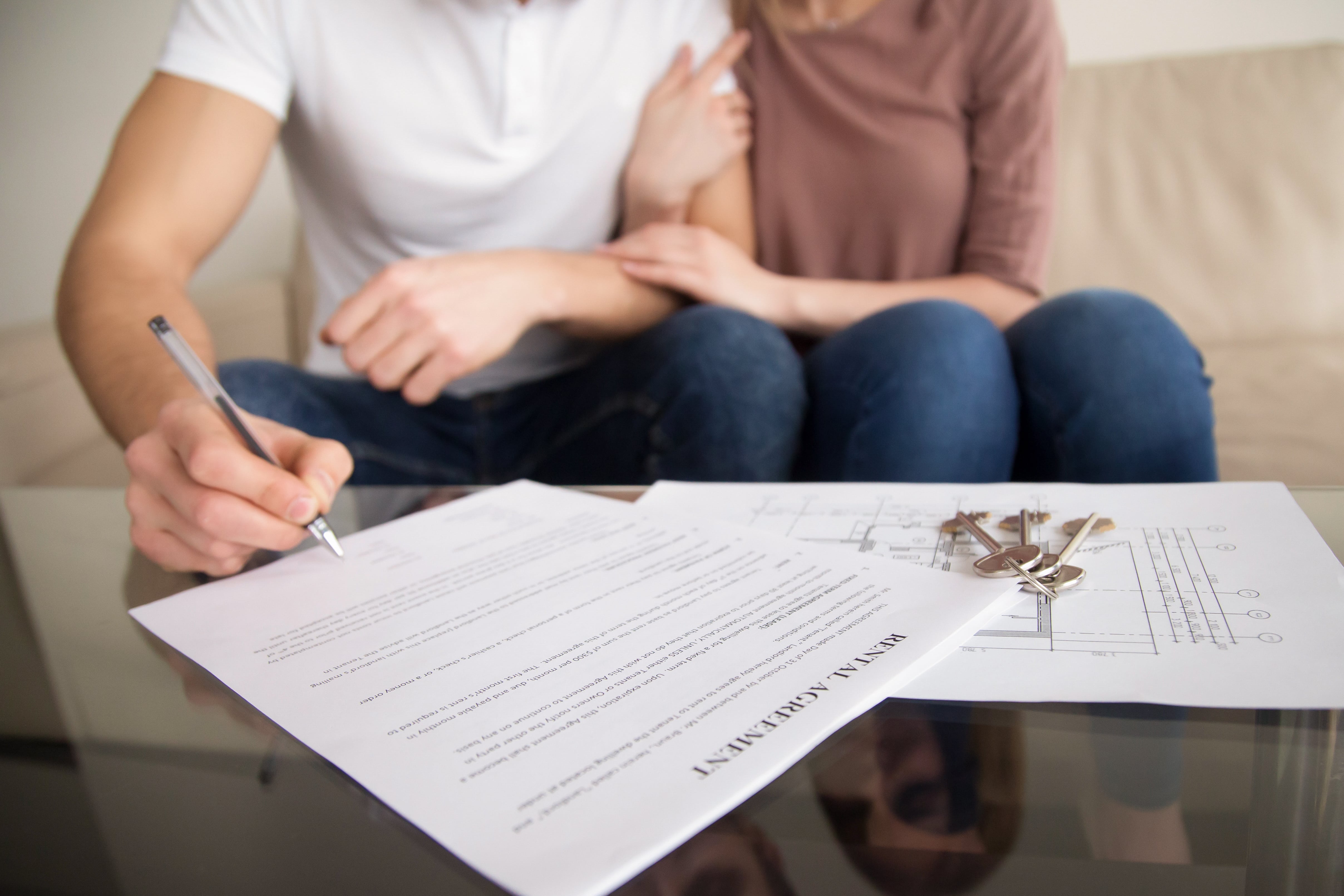 A couple signing a rental lease agreement with house keys and floor plans on the table, symbolizing the start of a landlord-tenant relationship.