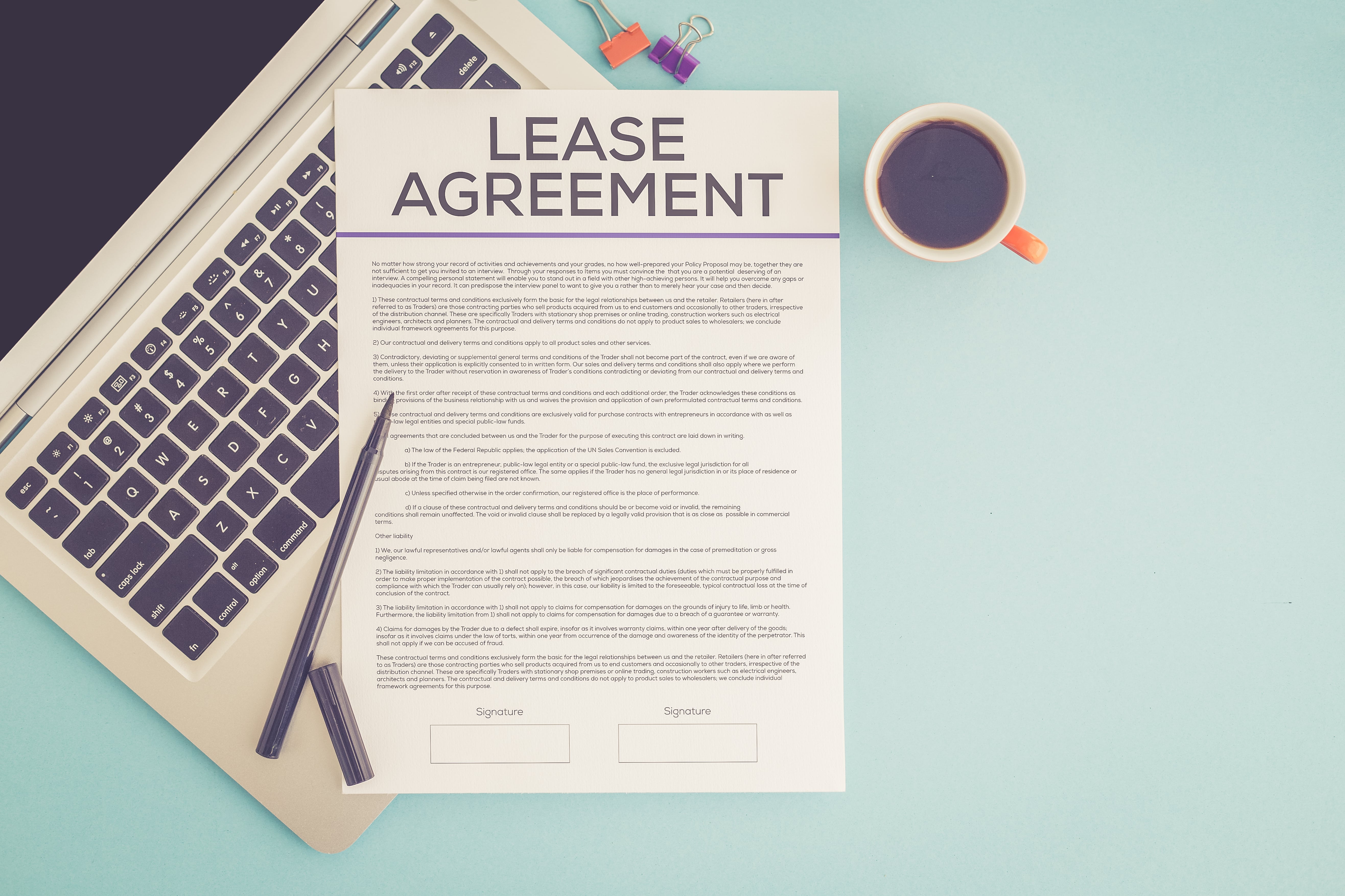 A lease agreement document on a laptop keyboard with a pen and a coffee cup, symbolizing rental contracts and legal agreements.