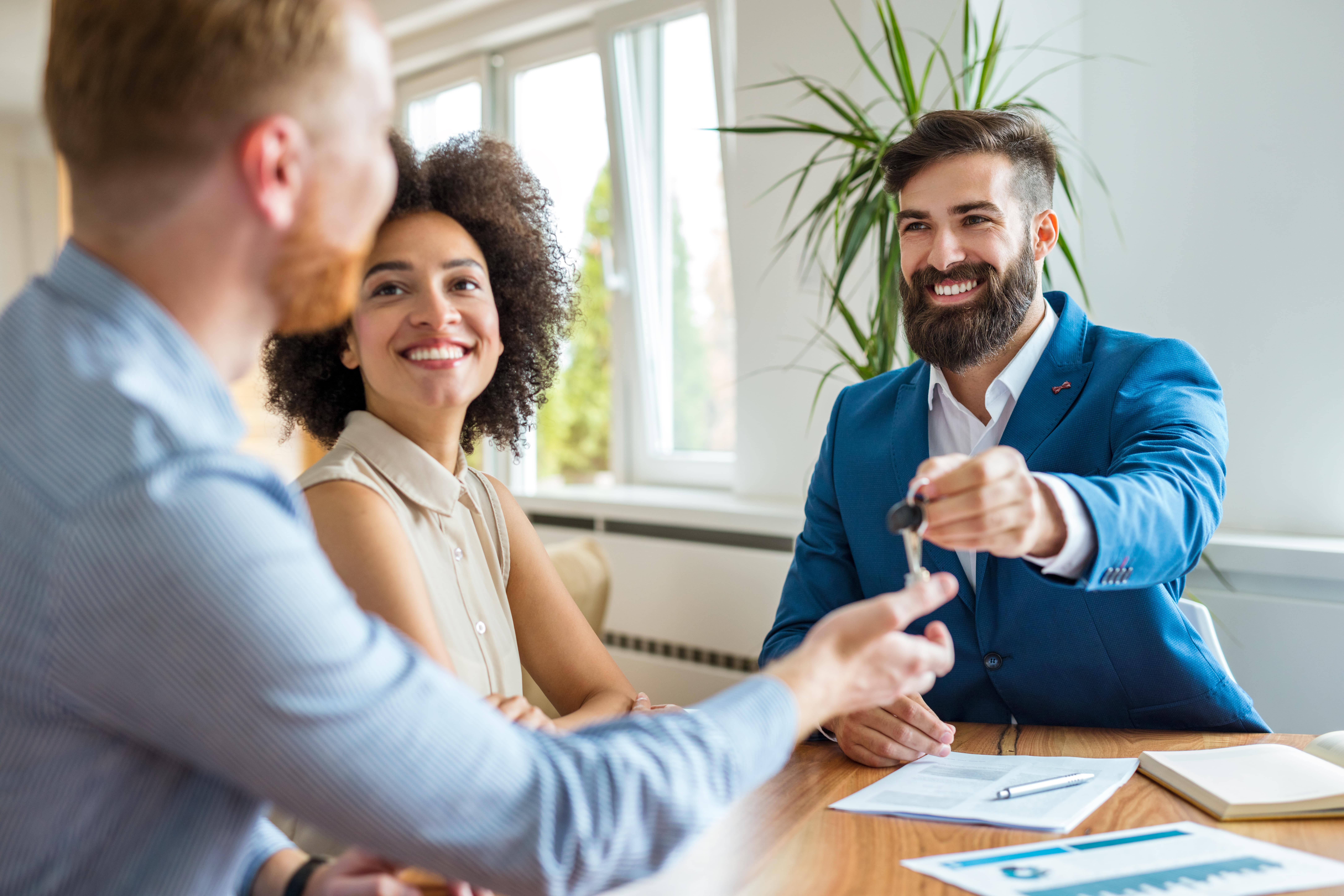 A real estate professional handing keys to new tenants in a bright apartment, illustrating the leasing process—one of the core tasks of a property manager.