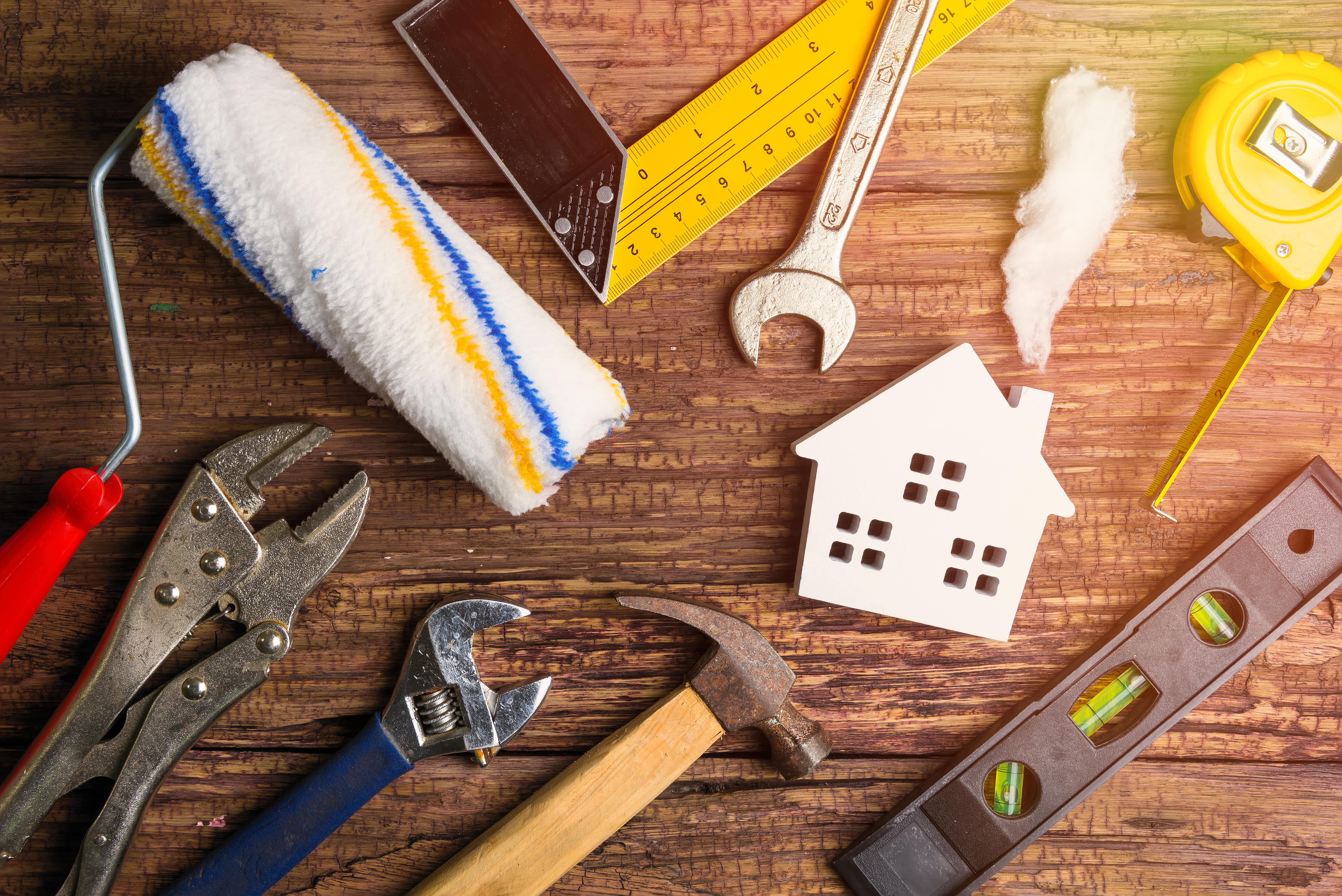 A collection of home improvement tools, including a paint roller, wrench, hammer, and a house model, symbolizing rental property maintenance and renovations.