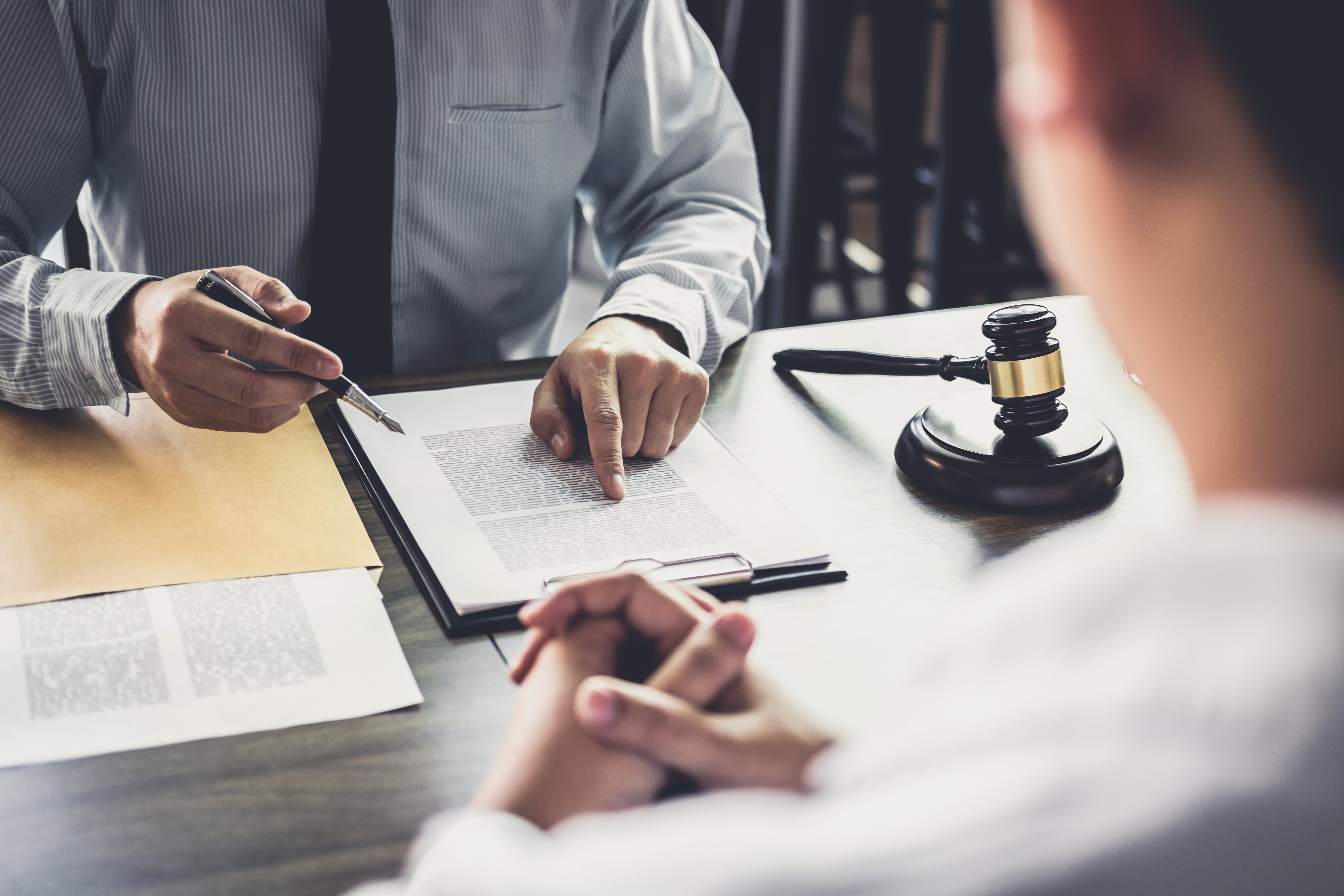 A legal professional pointing at a document while discussing terms with a client, with a judge’s gavel on the table, symbolizing legal guidance, lease agreements, and property management regulations.