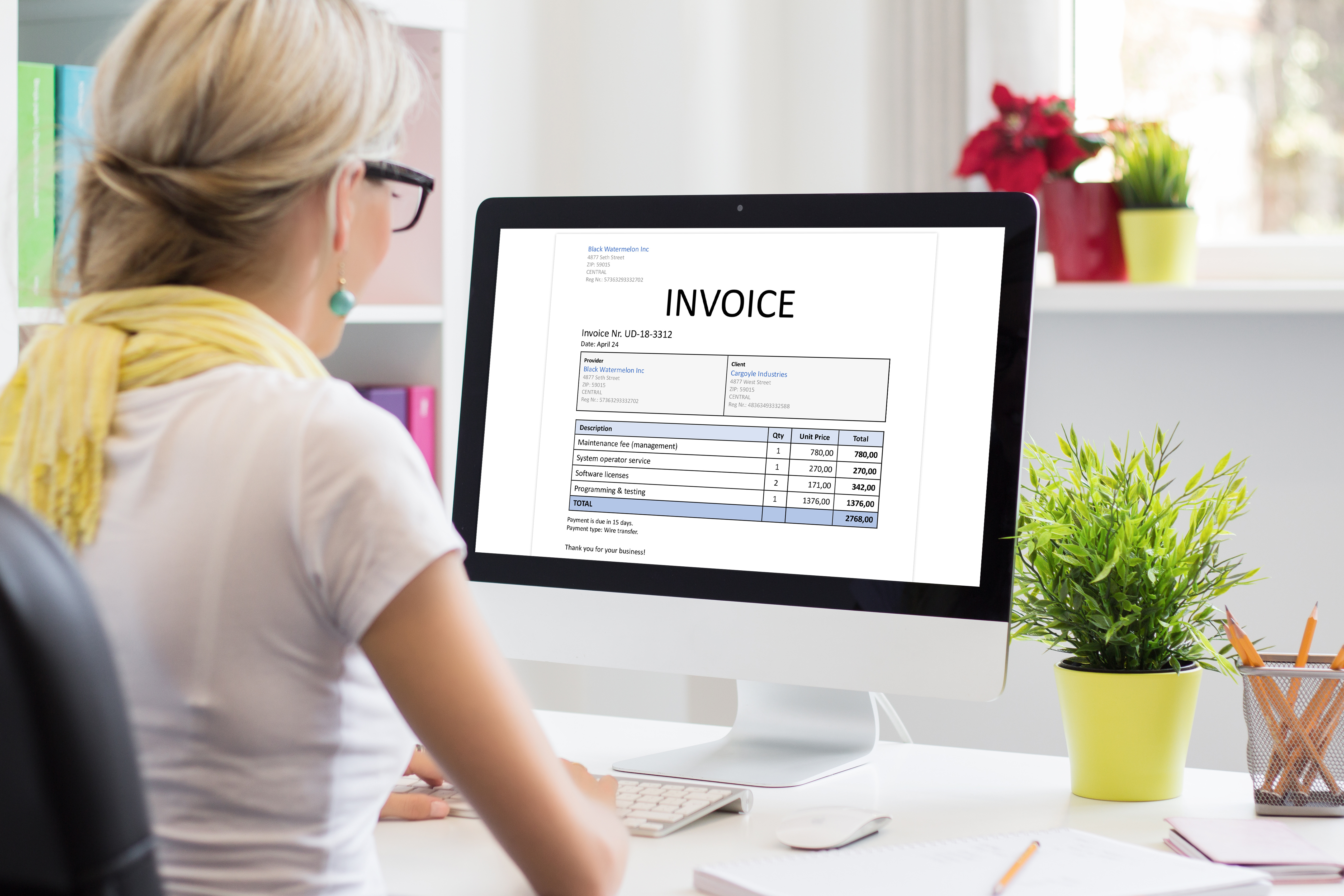 a blonde woman in a white shirt sitting a desk looking at an invoice on her computer with a yellow scarf on. 