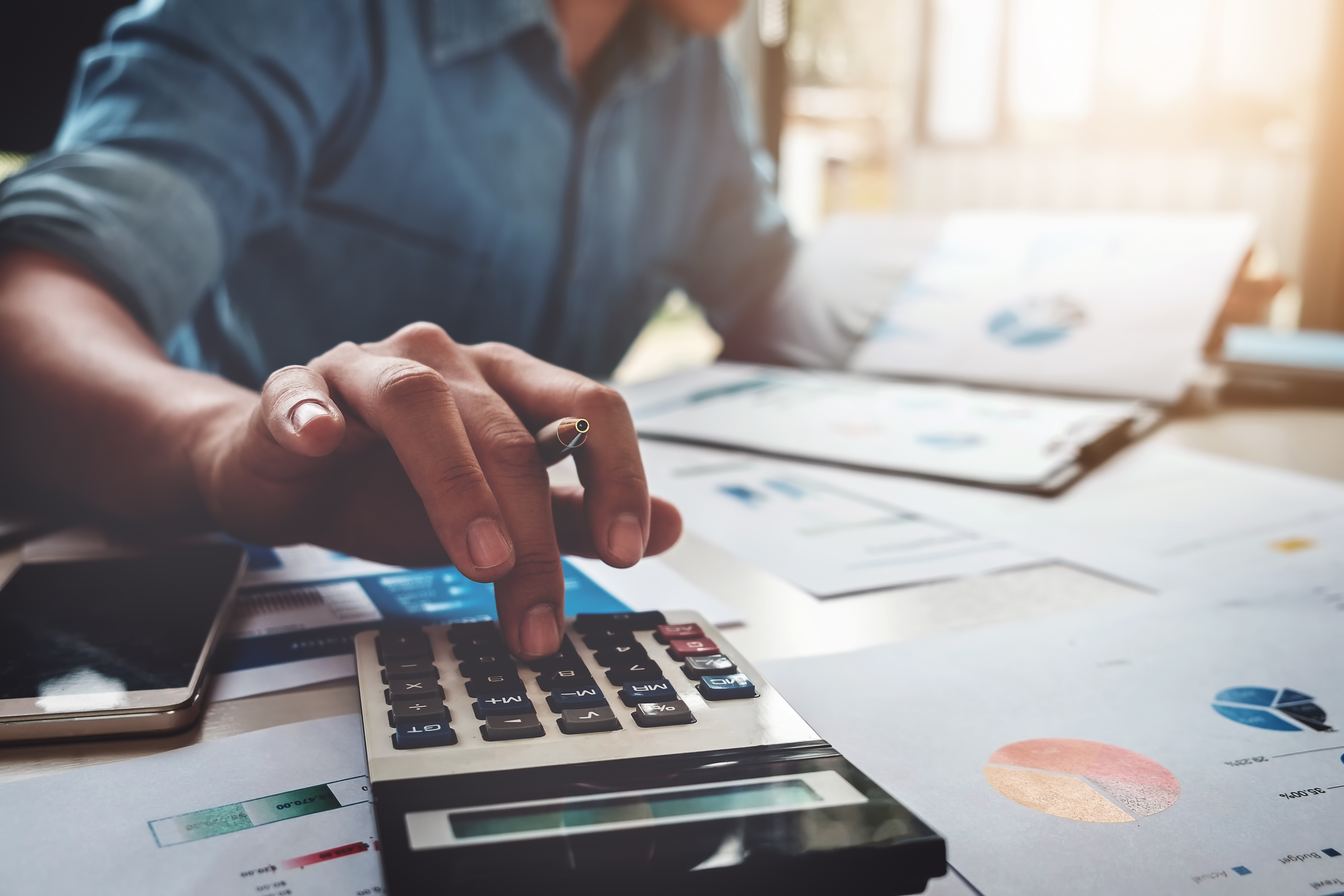 A person using a calculator to manage rental property finances with financial charts on the table.