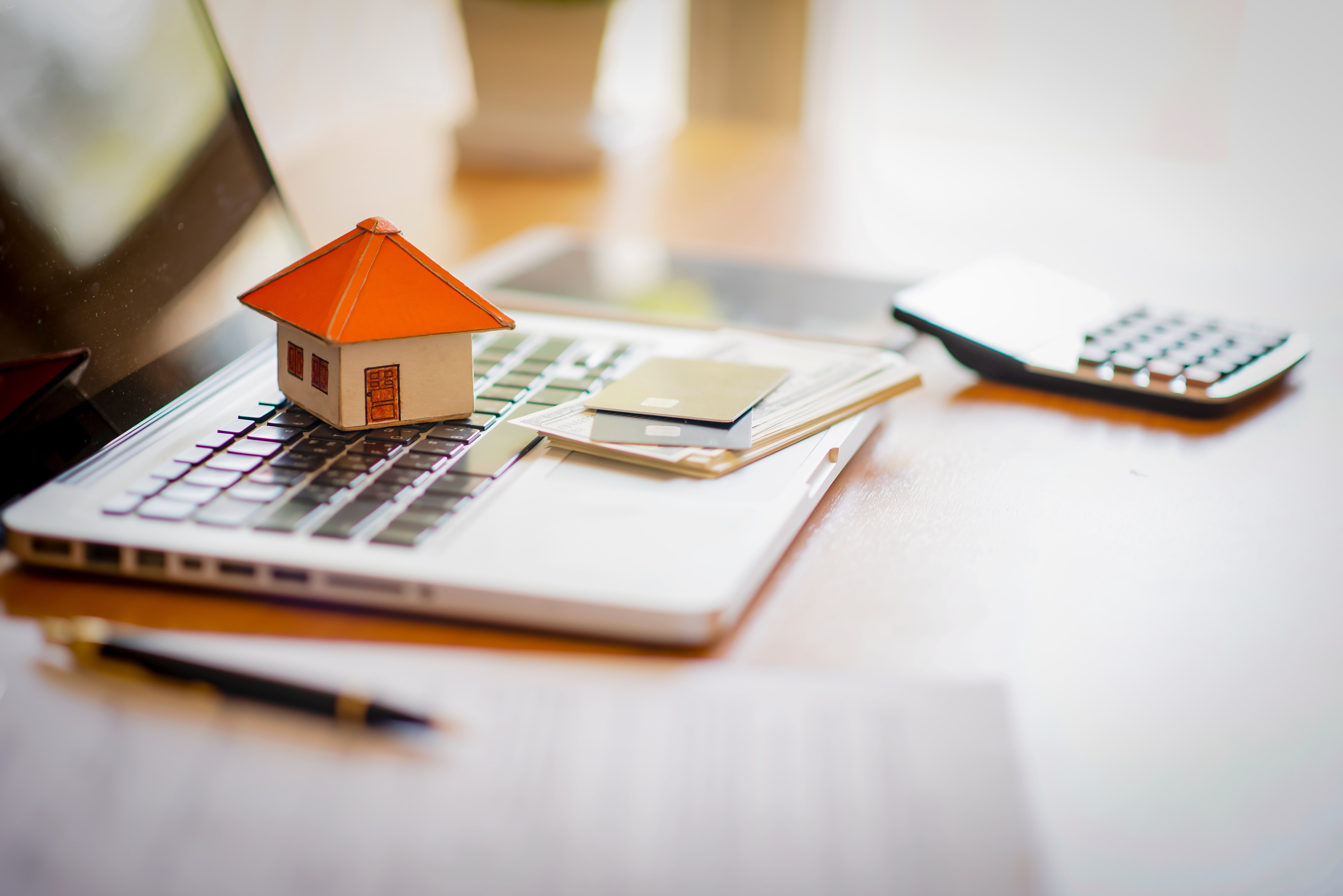 Small house model on a laptop keyboard with credit cards and a calculator, symbolizing online property management and real estate transactions.