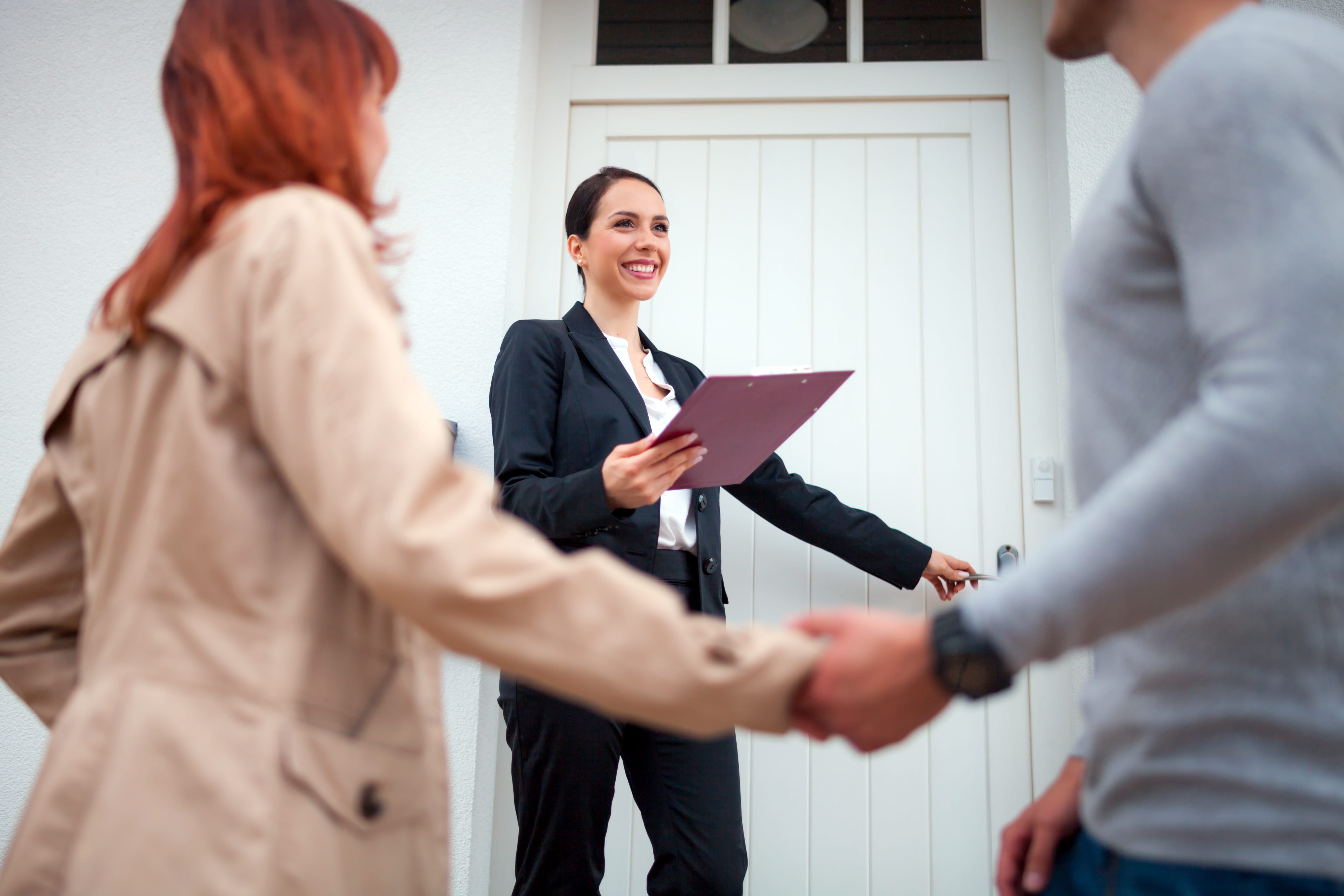 A professional real estate agent welcoming a couple to a property viewing at the front door.