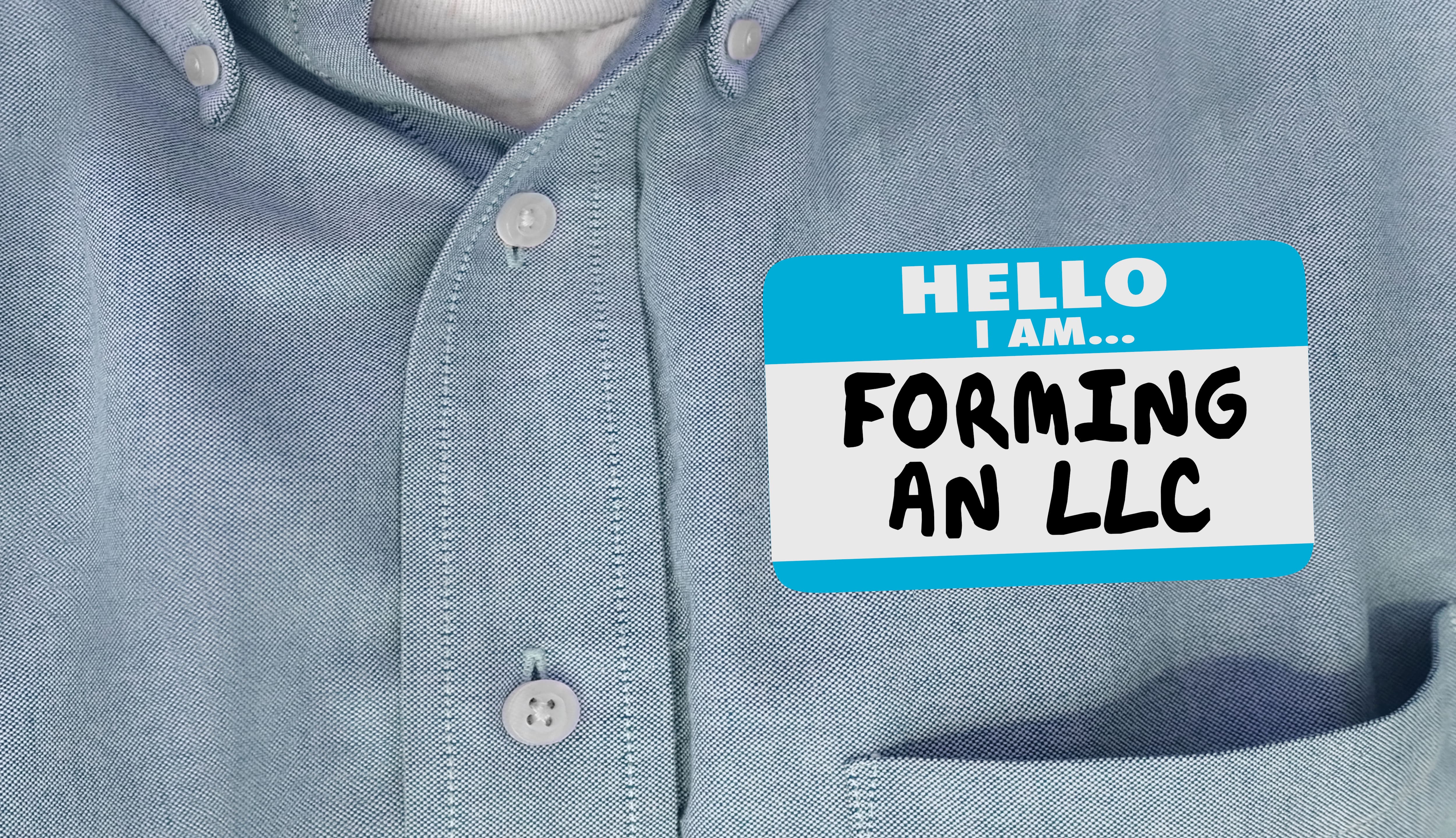 A name badge reading ‘Hello I am… Forming an LLC’ pinned to a light blue shirt, symbolizing the process of starting a business entity.