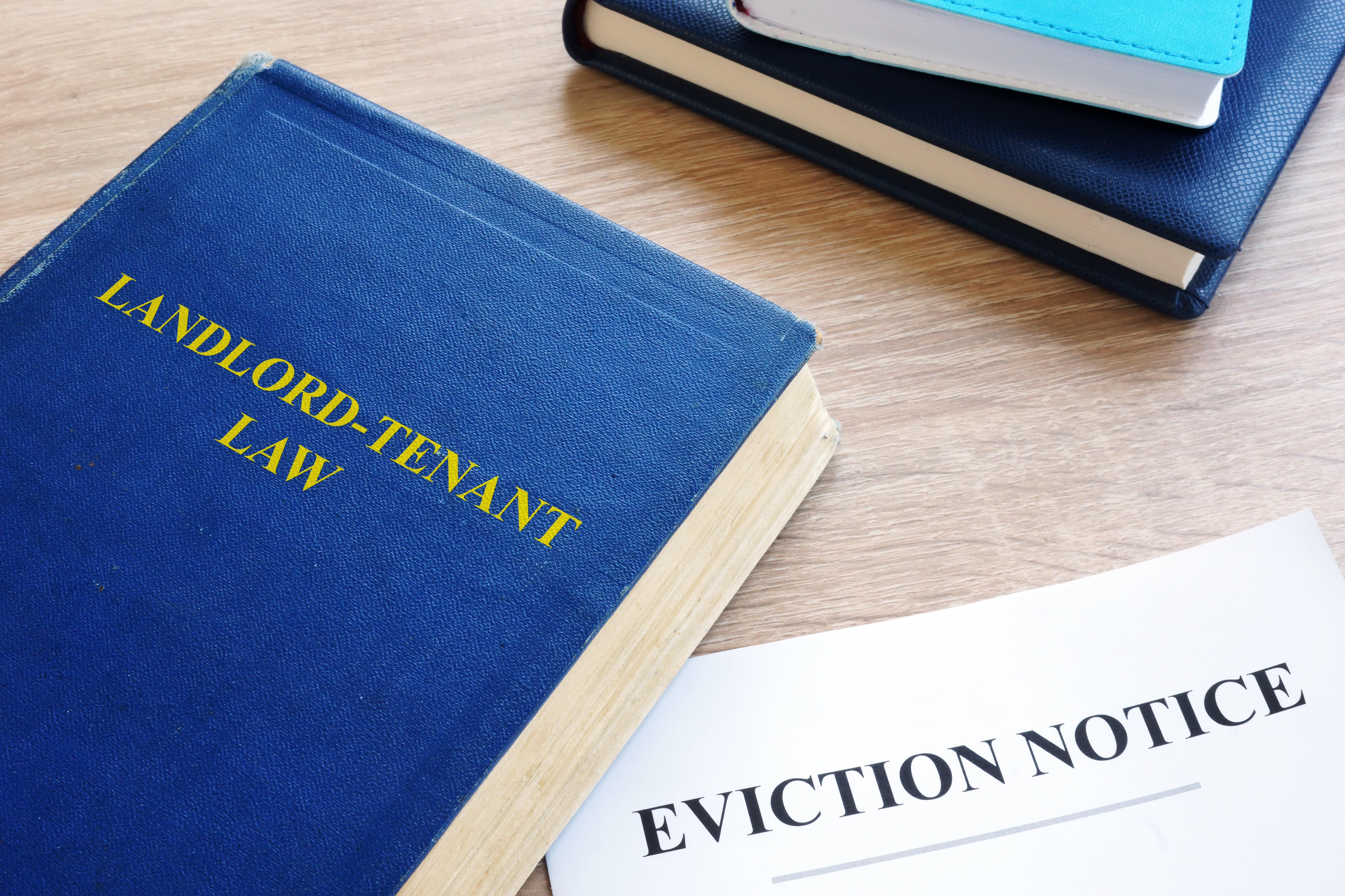 A blue book titled ‘Landlord-Tenant Law’ resting on a wooden desk next to an eviction notice, representing legal aspects of tenant and landlord rights.