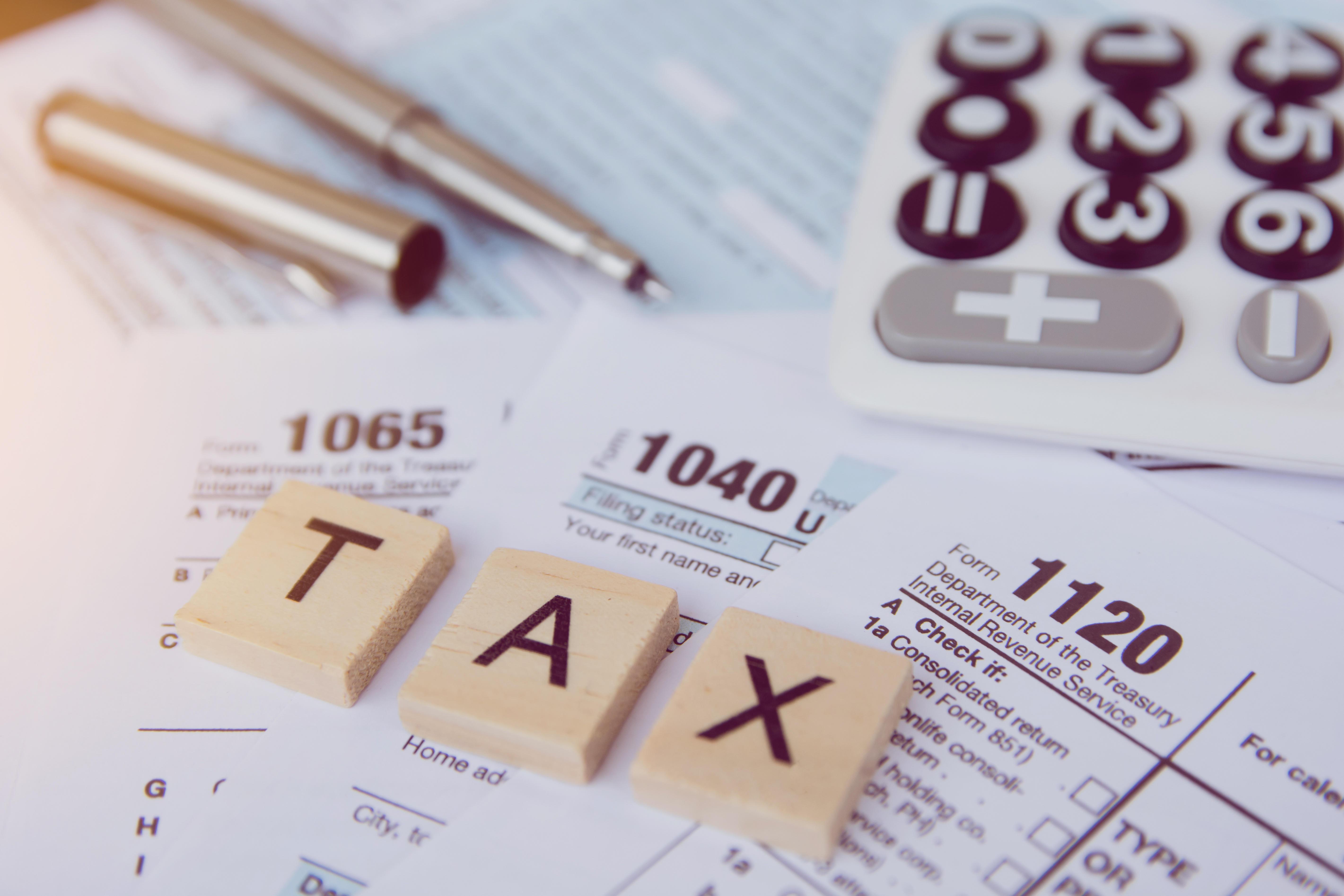 Tax documents, a calculator, and ‘TAX’ spelled with wooden blocks, representing rental property tax deductions.