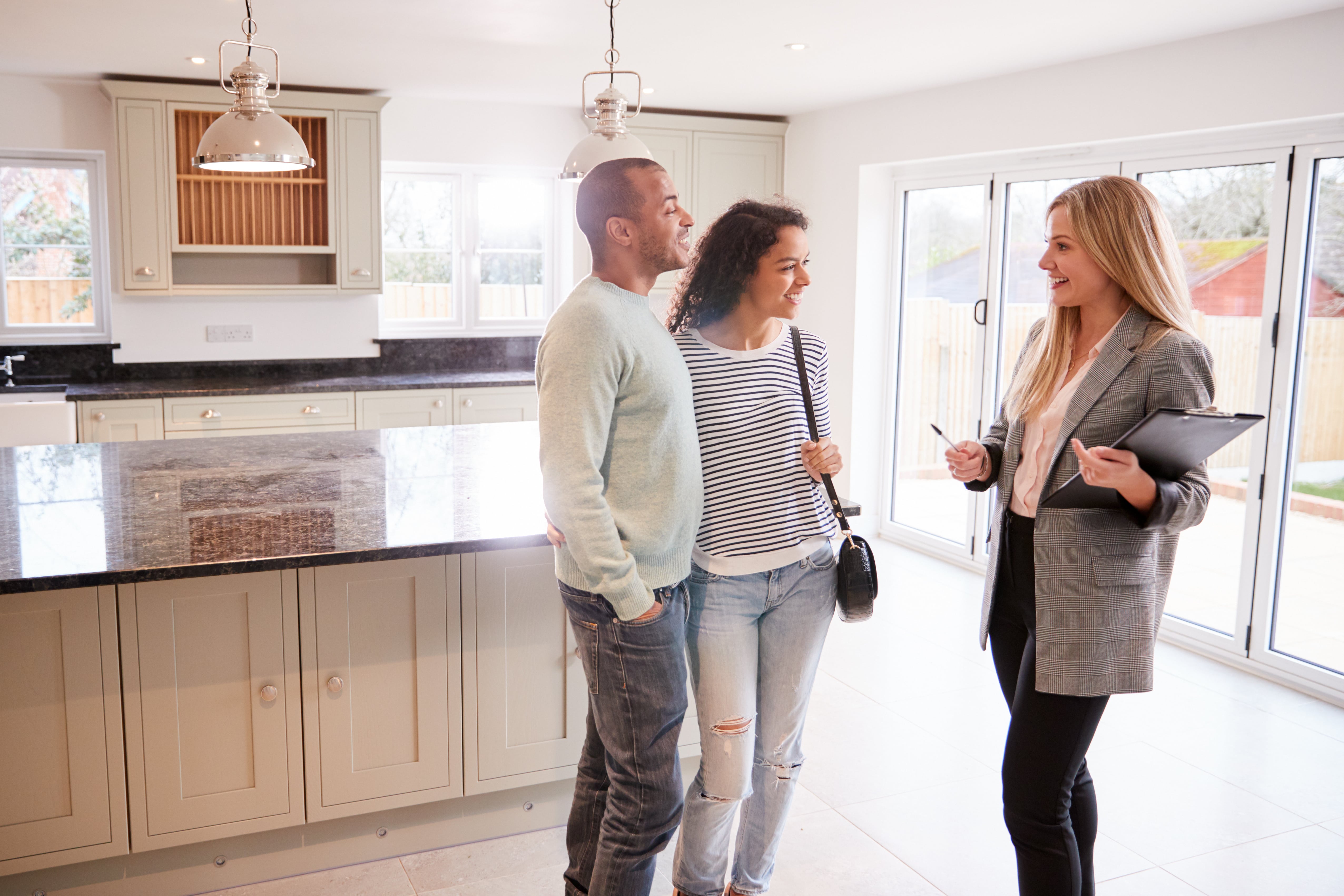 A smiling real estate agent showing a happy couple a modern kitchen during a home tour.