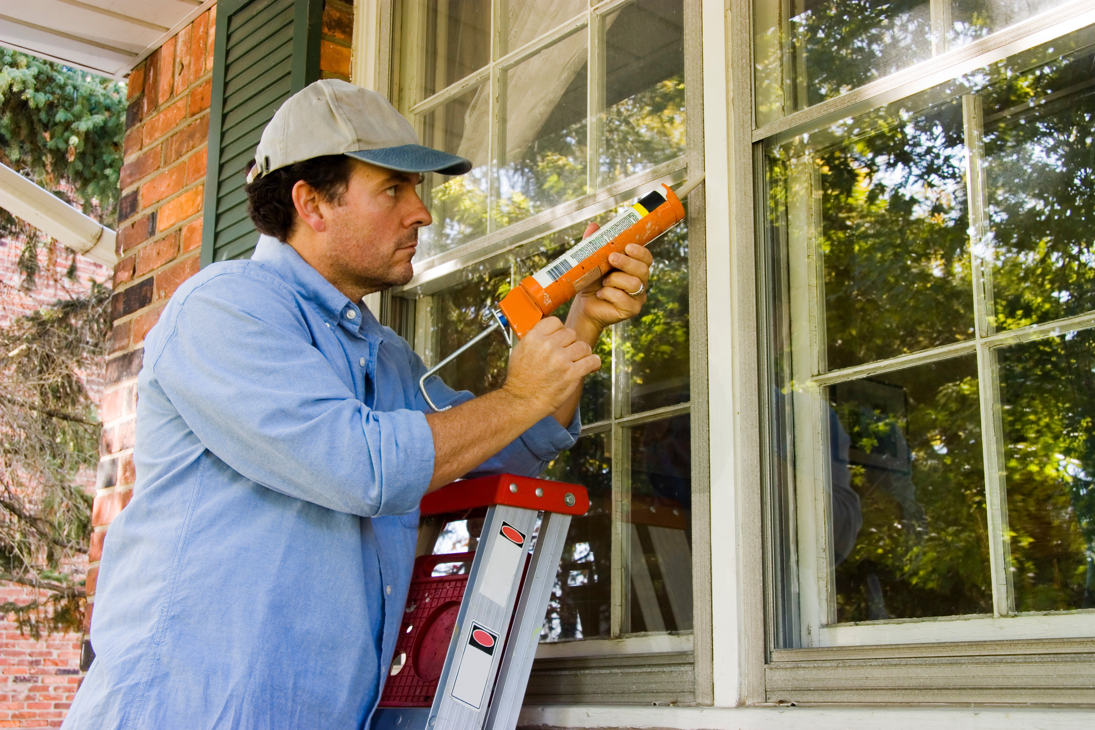 A man applying caulking around a window, performing maintenance or repair work on a house.