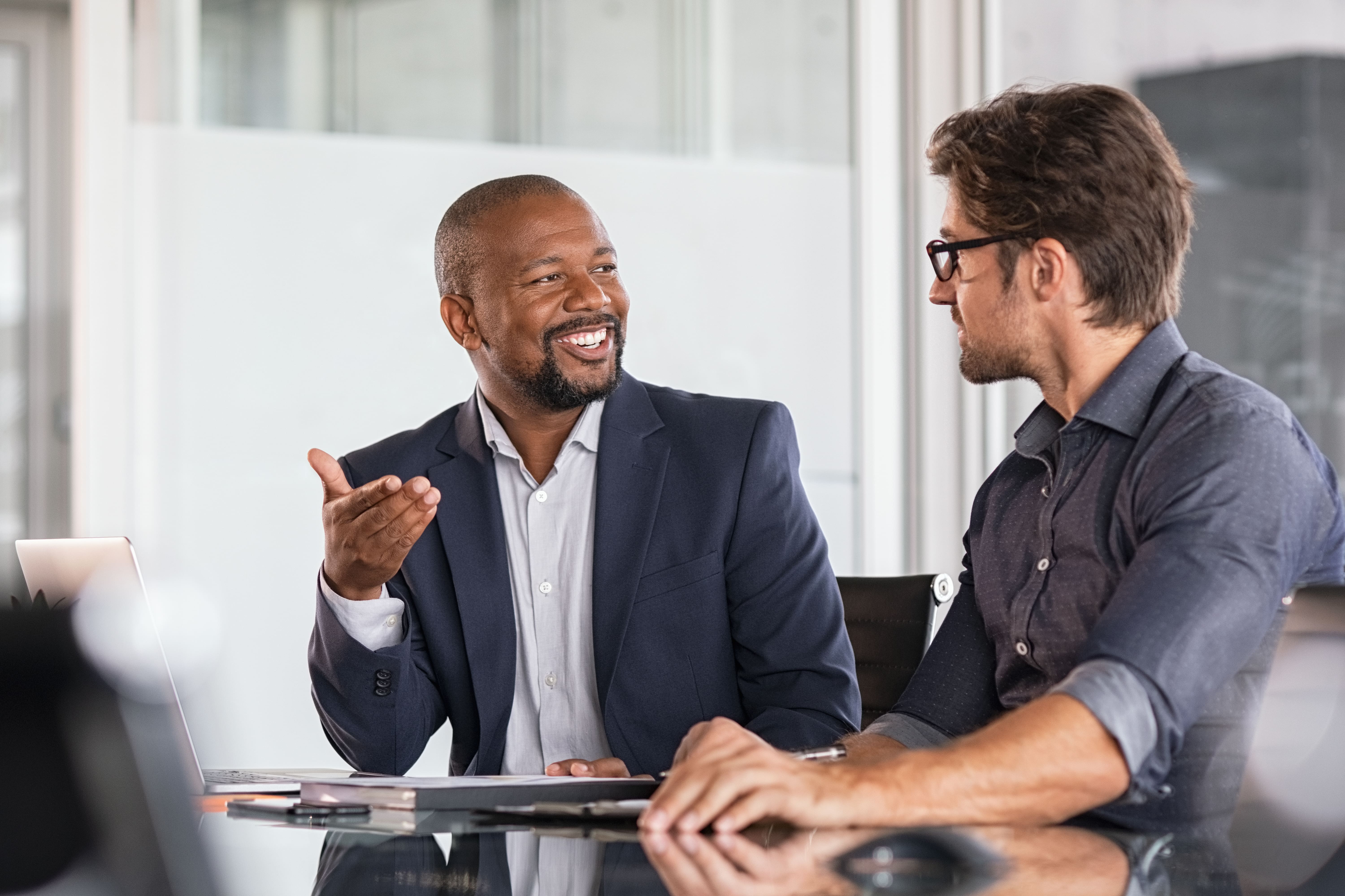 Two business professionals in a modern office, engaged in a conversation, representing property management consulting, client relationships, and strategic real estate discussions.