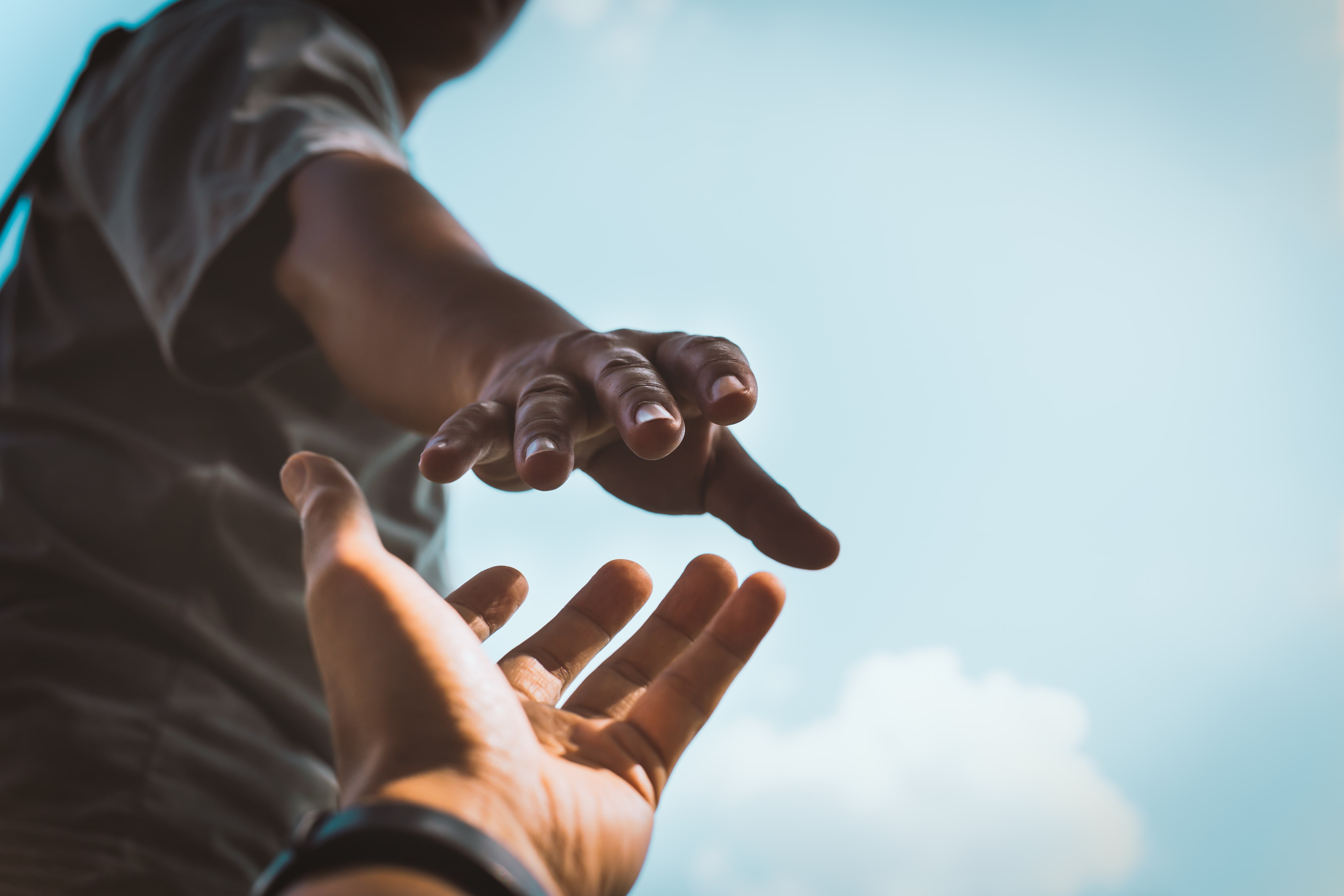 Two hands reaching out to each other against a blue sky, symbolizing assistance, support, or teamwork.