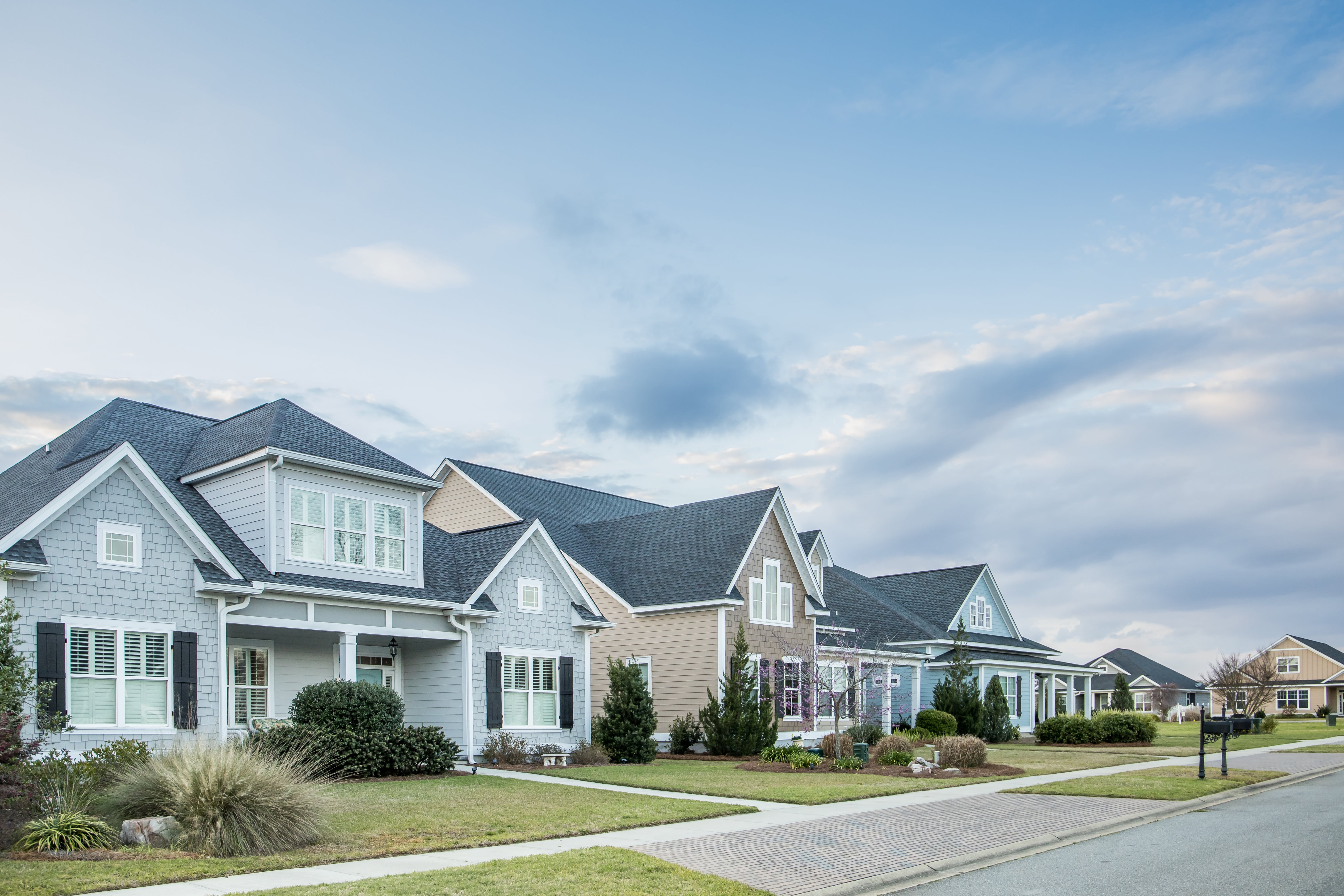 A row of modern suburban houses with well-manicured lawns and a blue sky. The homes feature diverse architectural styles, conveying a sense of community.