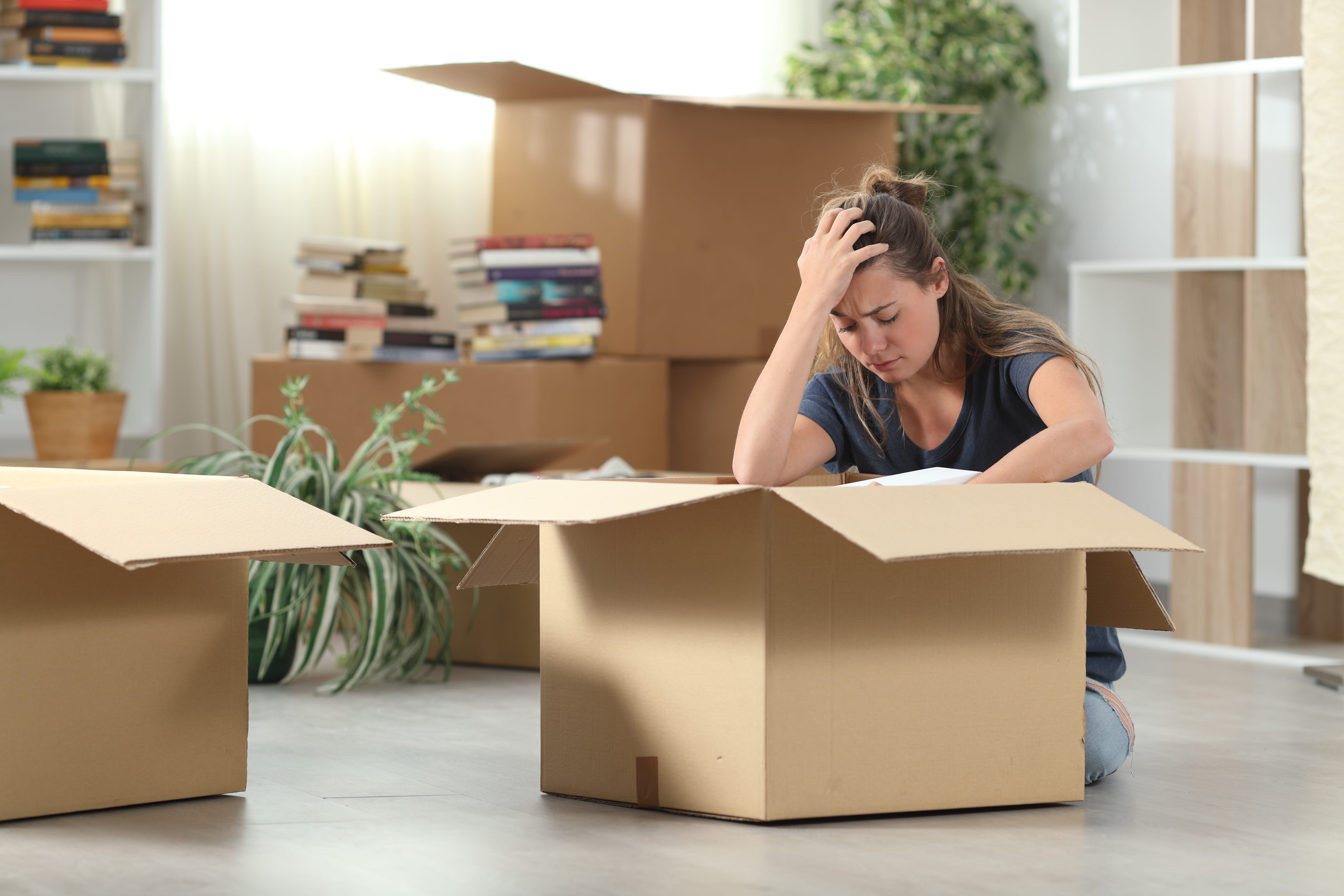 A stressed woman sitting on the floor surrounded by moving boxes, symbolizing the challenges of eviction or moving out.