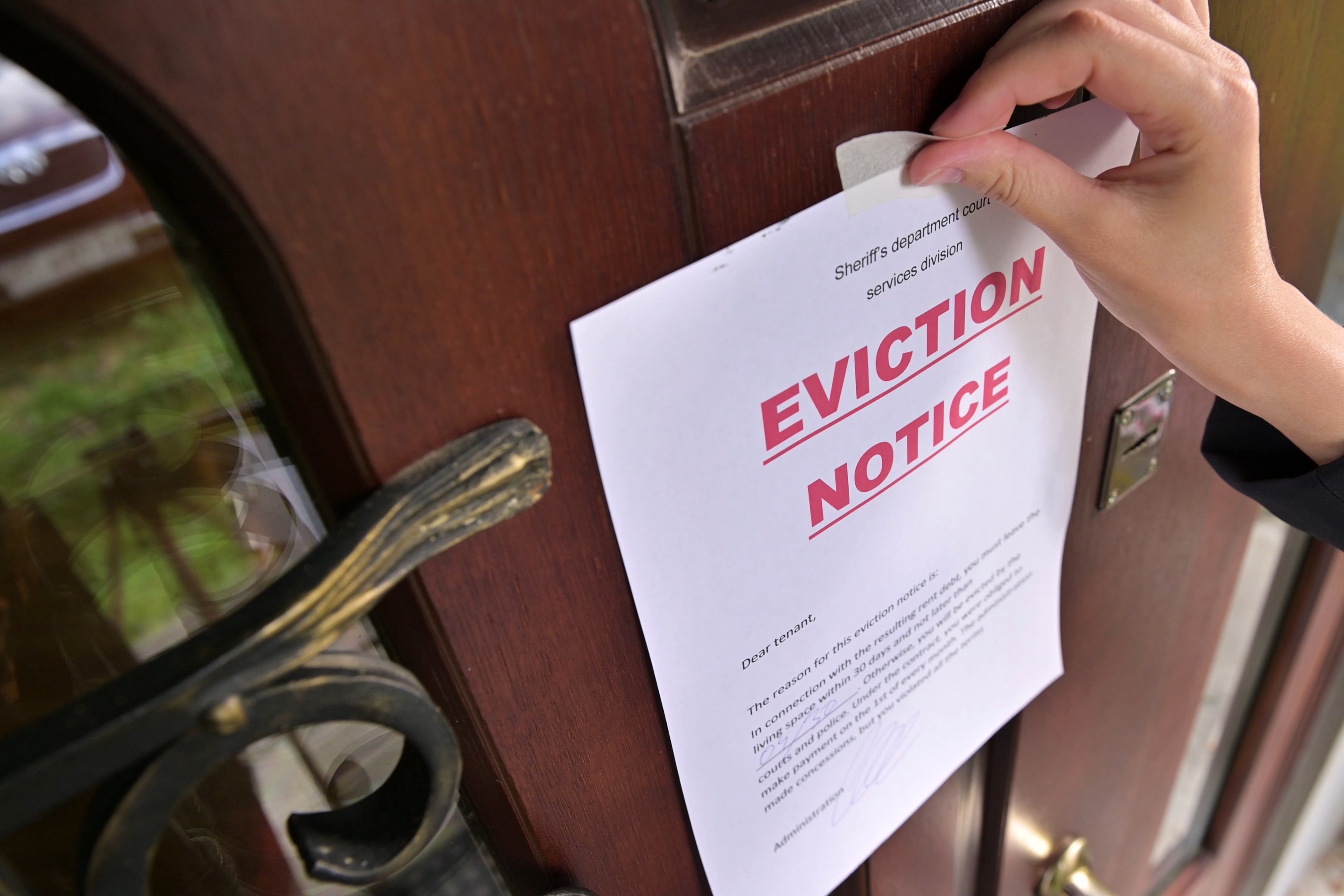 A close-up of an eviction notice being taped to a wooden door, representing the legal process of tenant removal.