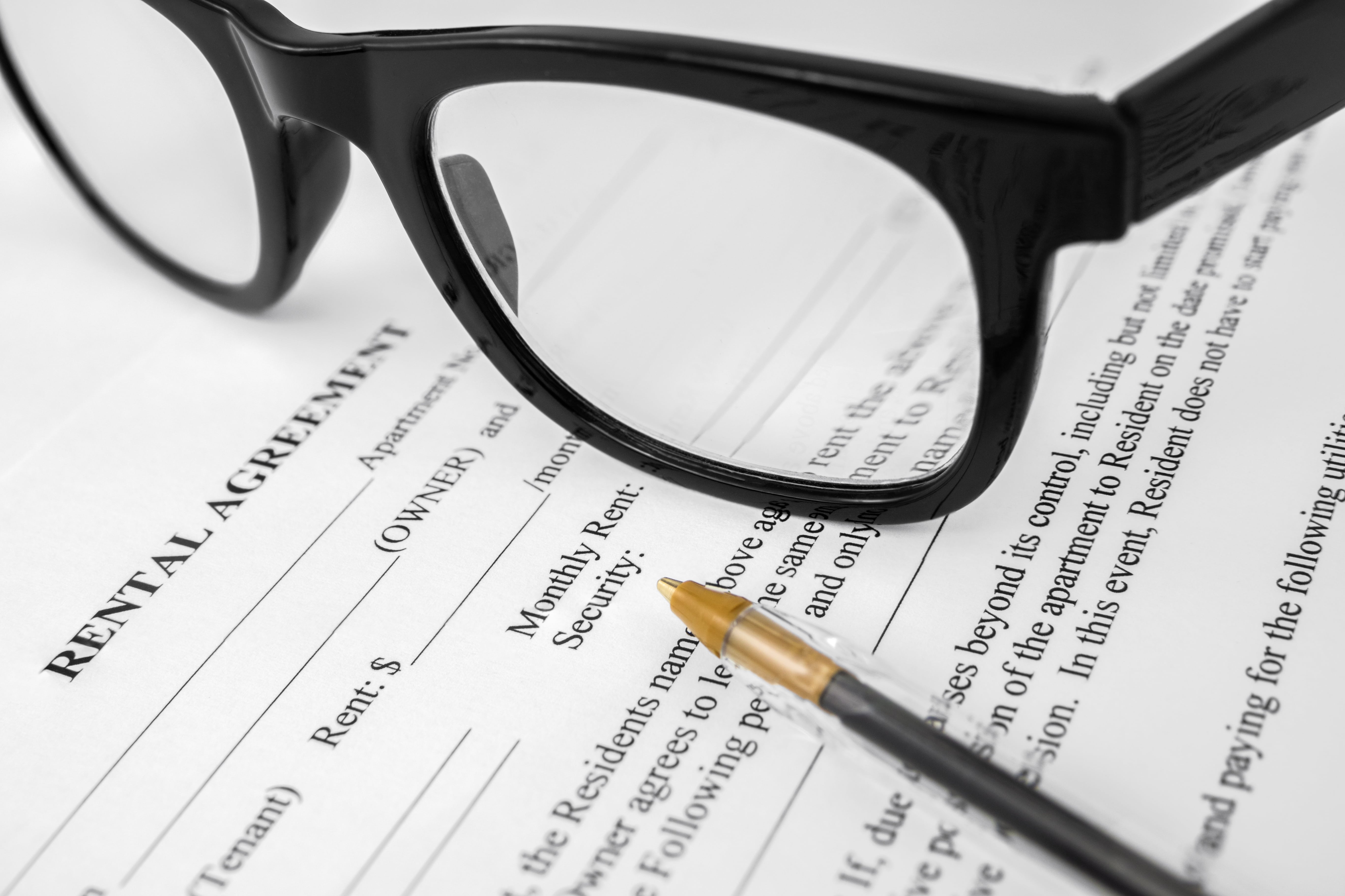 Close-up of a rental agreement document with glasses and a pen, symbolizing lease terms and rental contracts.