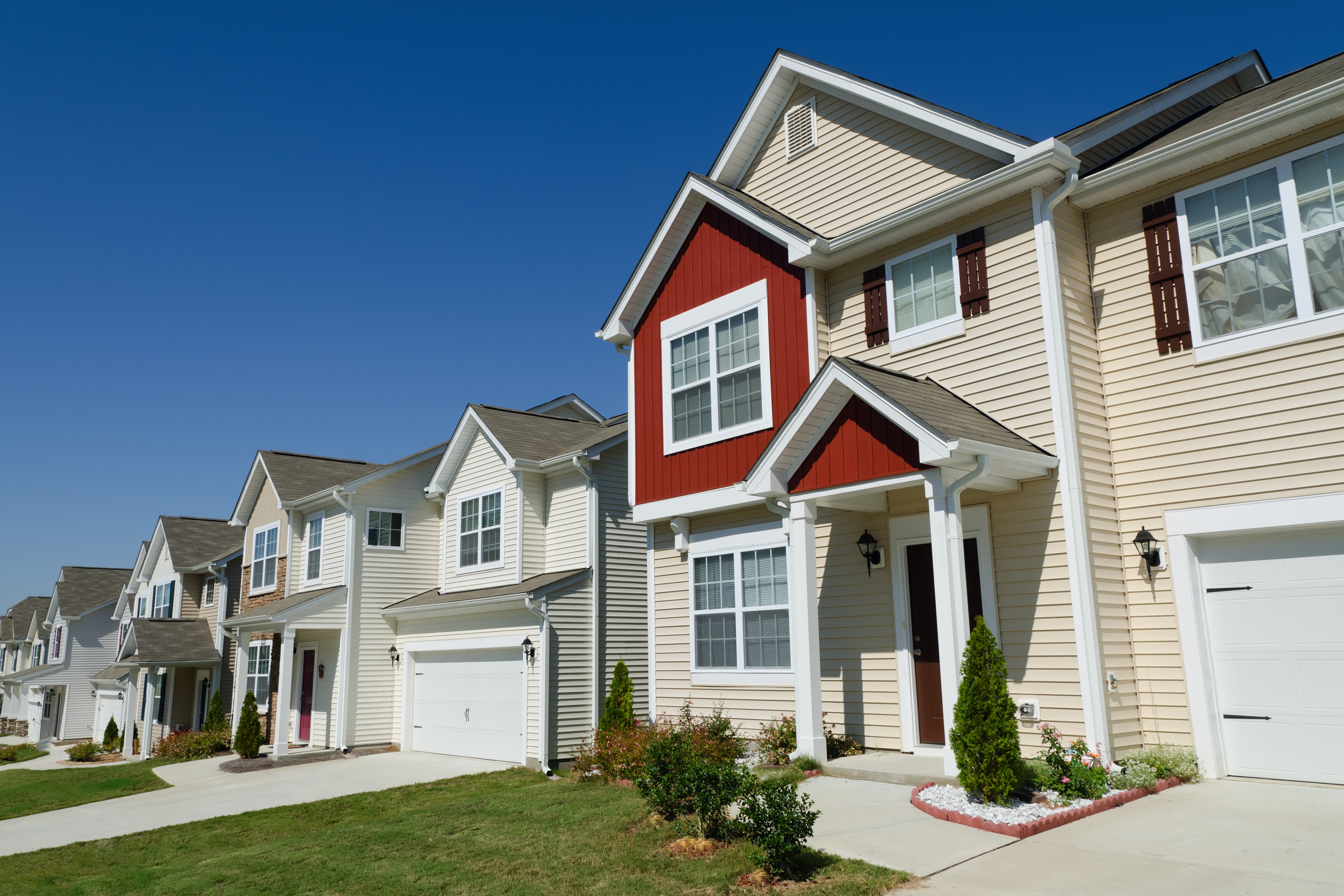 A row of modern suburban townhouses with well-maintained landscaping under a clear blue sky, representing residential real estate and property investment opportunities in Florida.