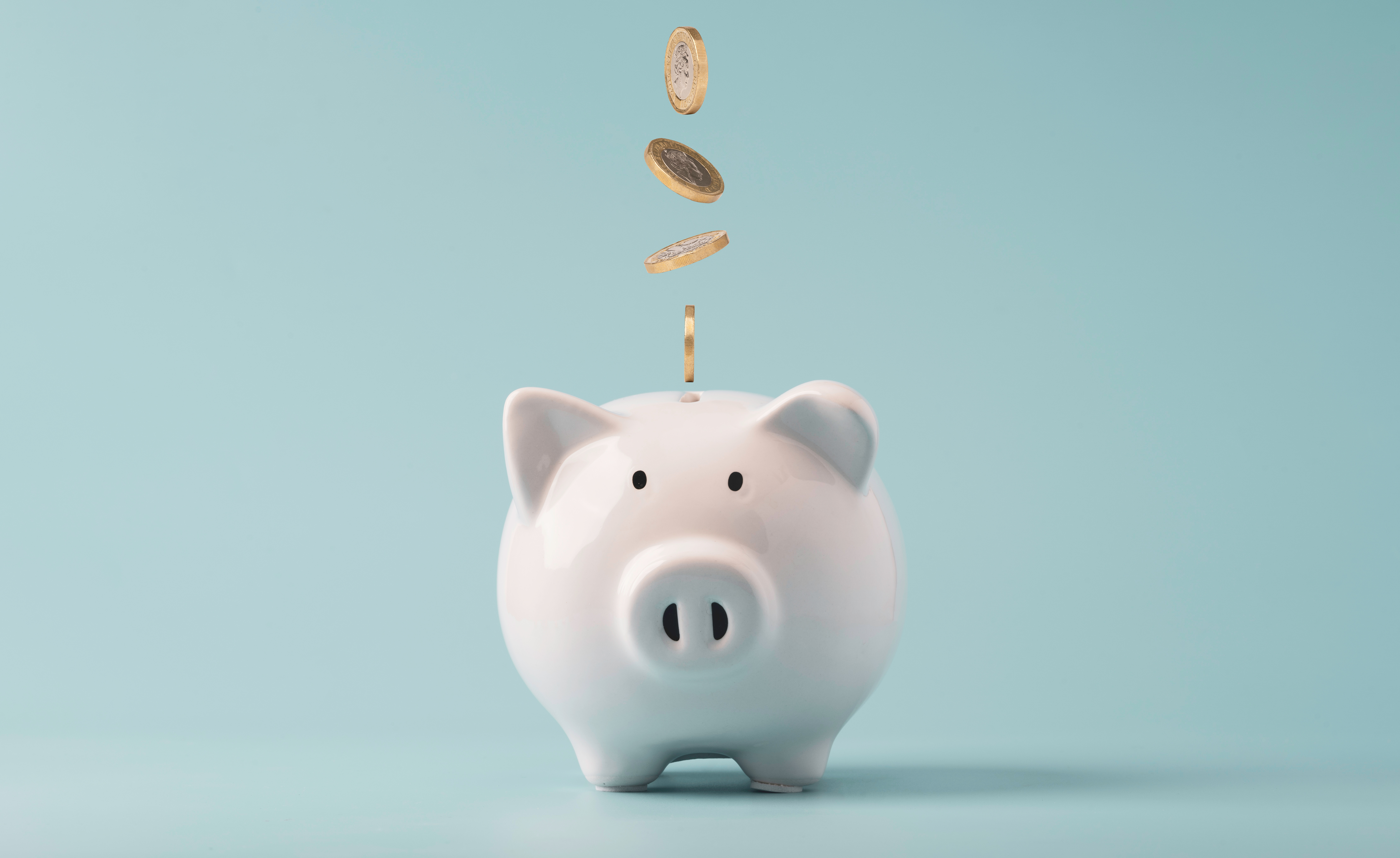 A white piggy bank with coins being dropped into it against a light blue background.