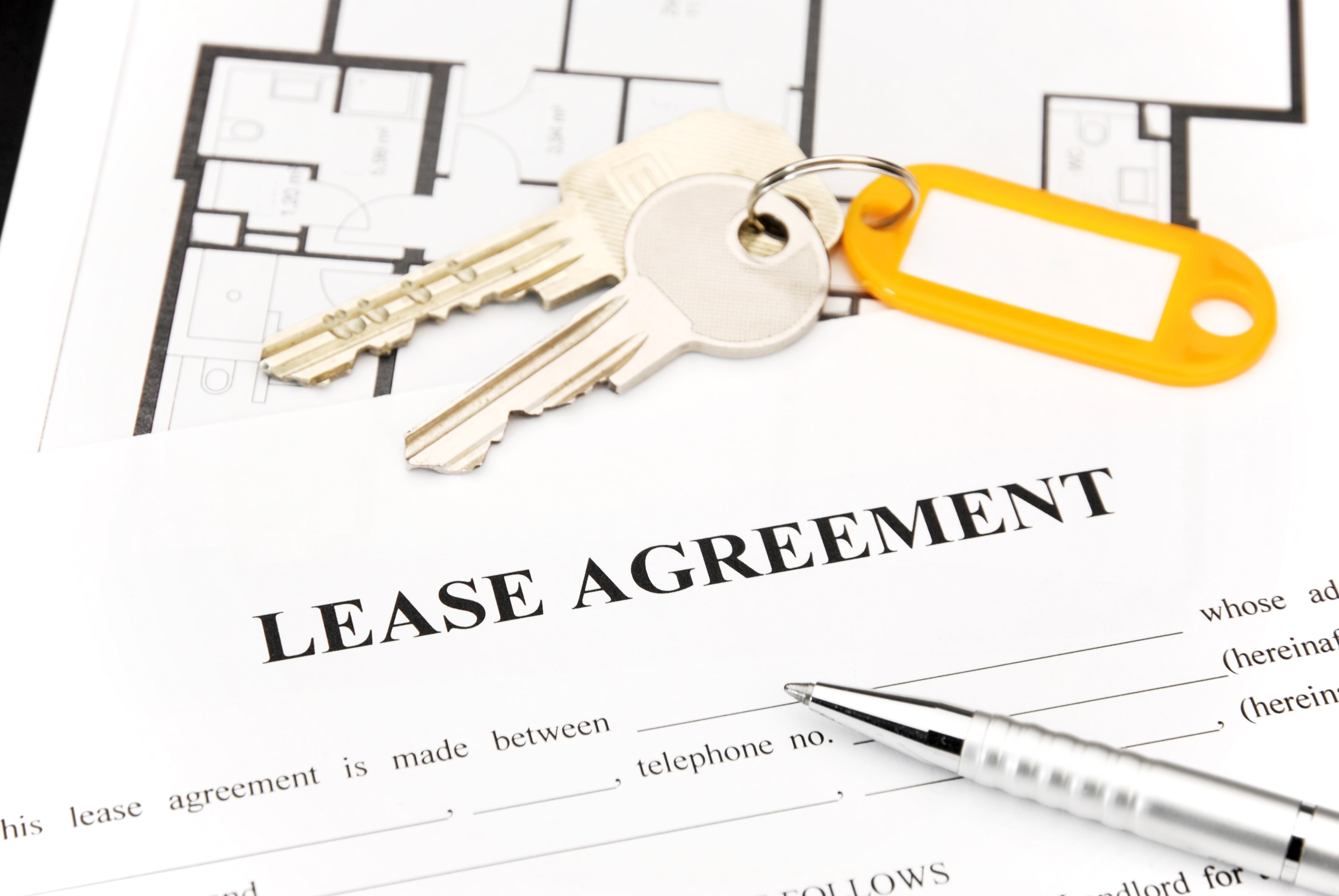 Close-up of a lease agreement document with a silver pen and a set of house keys on top, symbolizing rental contracts and property management.