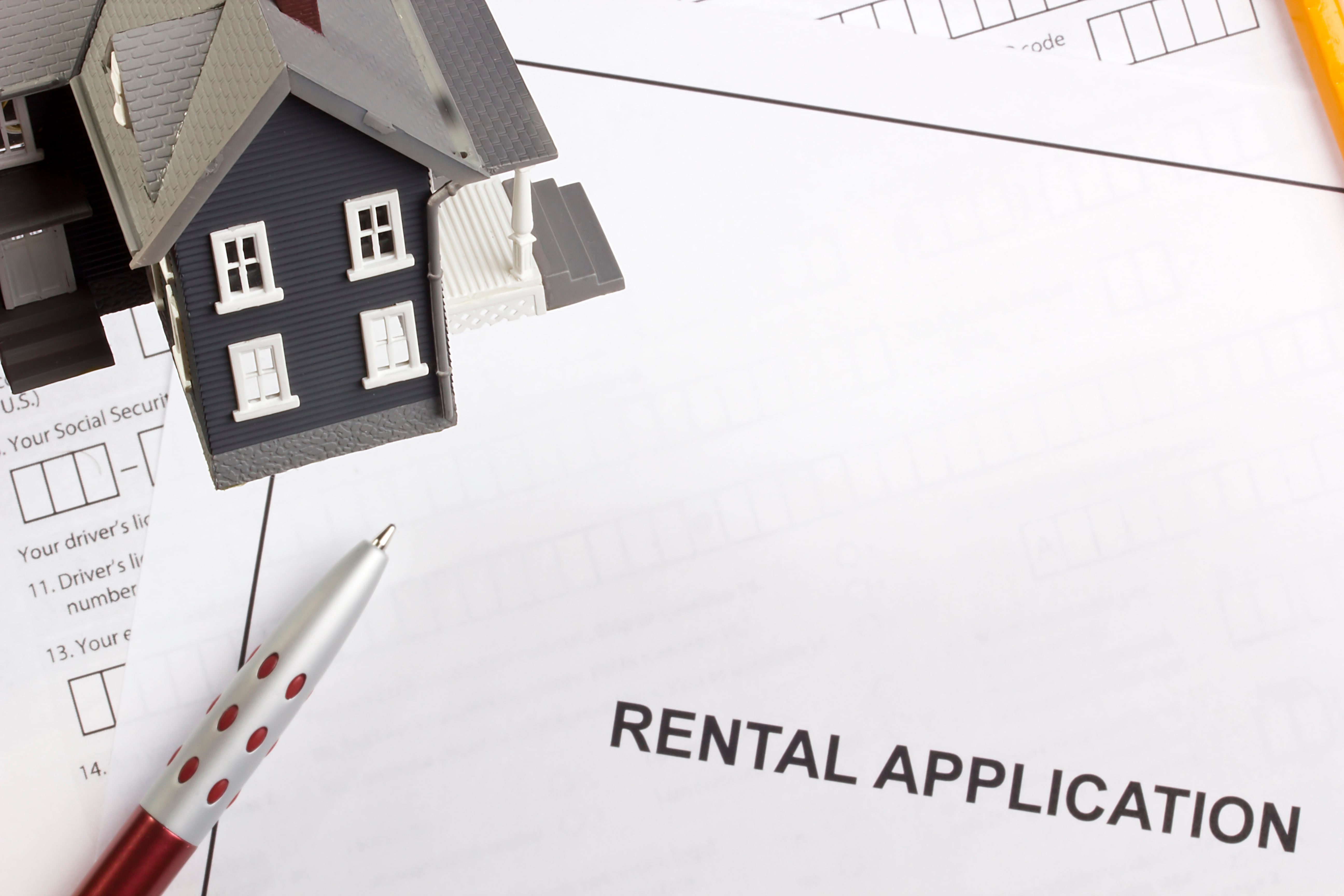 Rental application form with a model house and pen, symbolizing tenant screening and fair housing compliance.