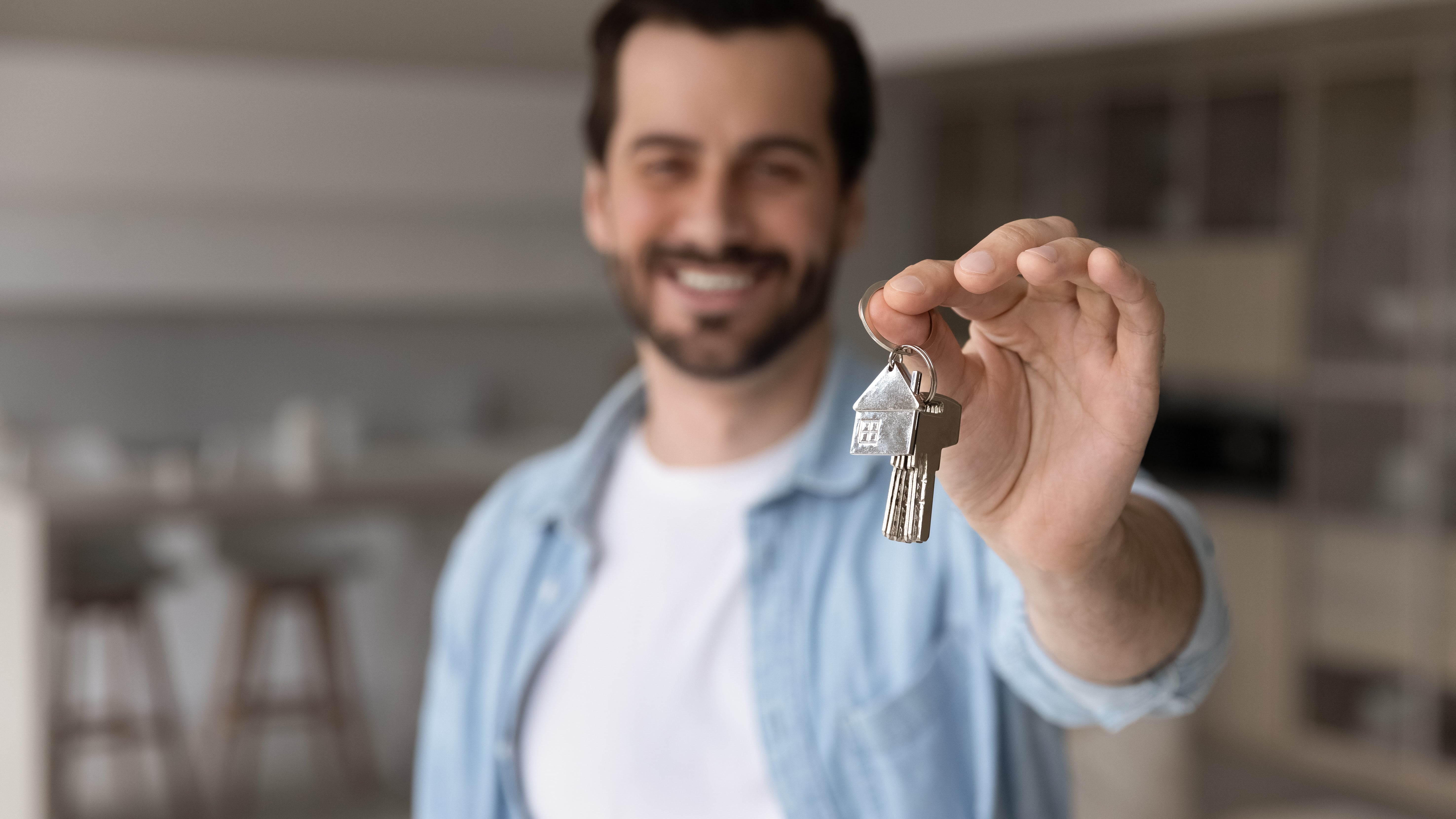 A smiling man holding house keys in the foreground, symbolizing a successful lease renewal and tenant retention.