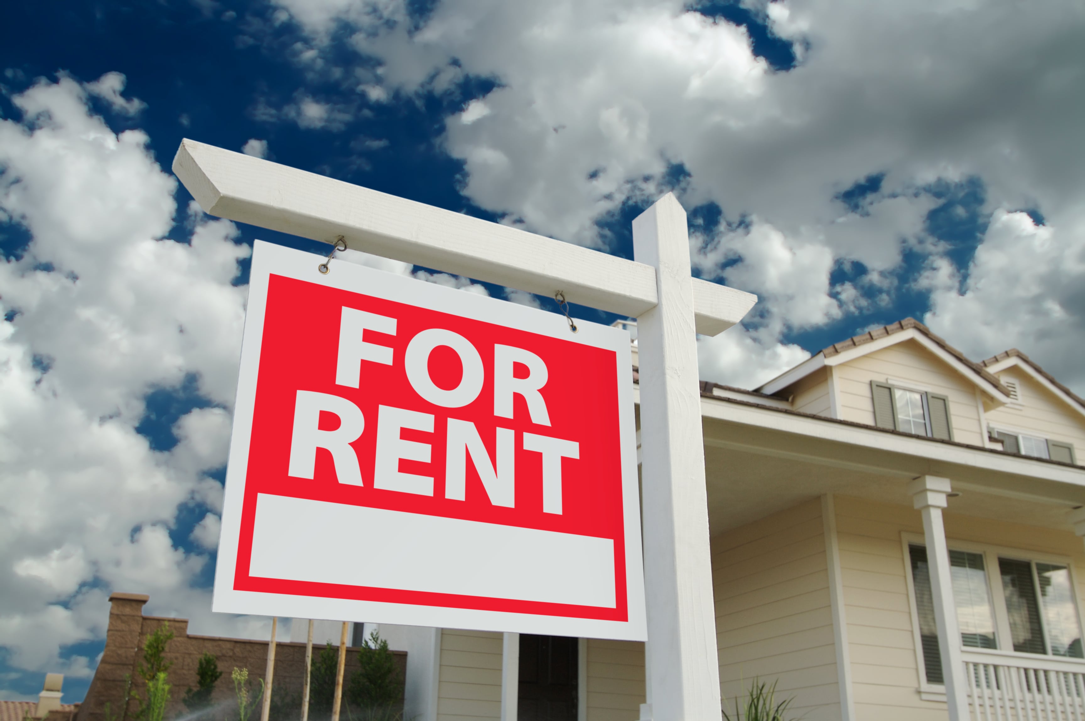 Large red and white ‘For Rent’ sign in front of a suburban home with a bright sky in the background, representing property rentals and real estate opportunities.