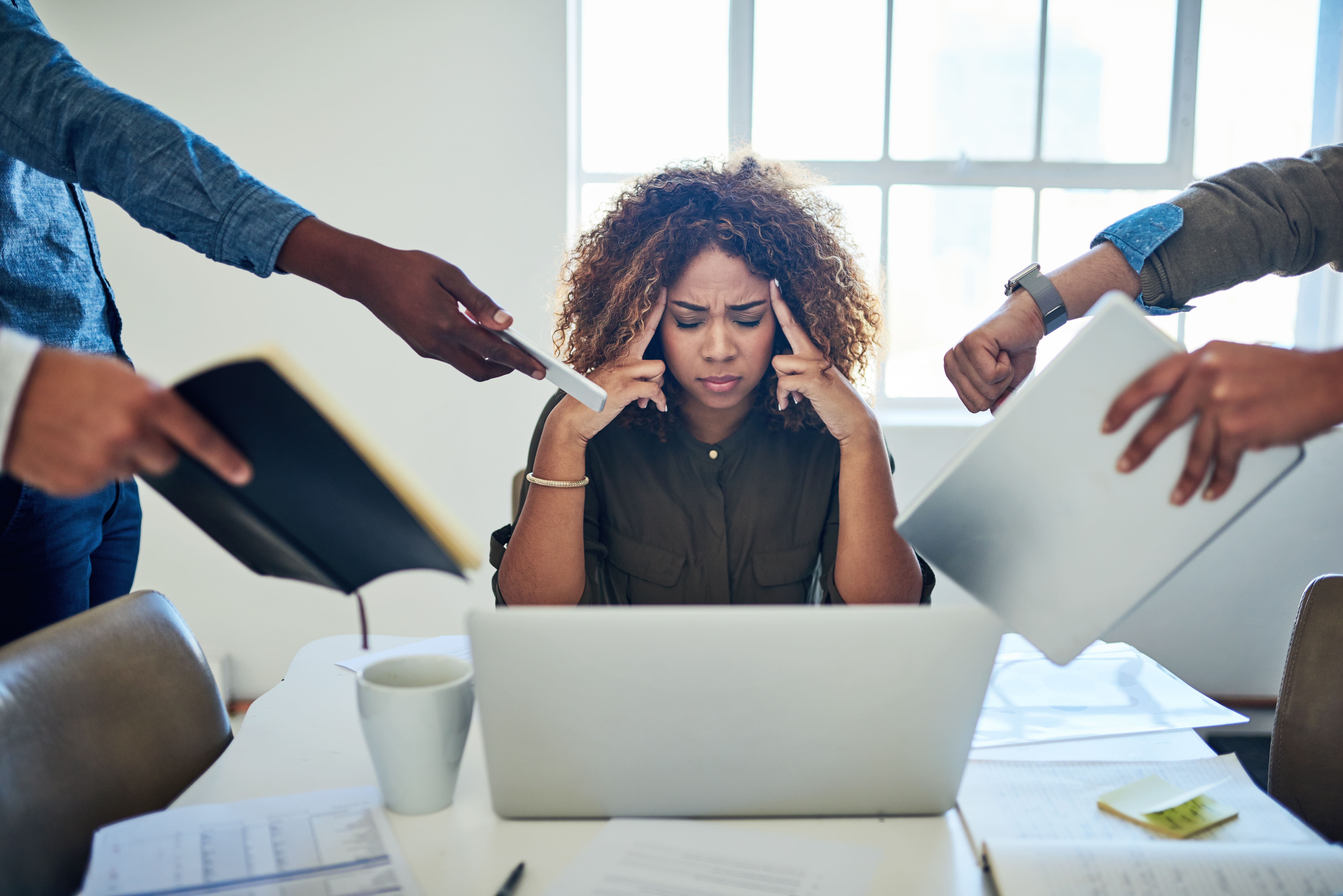 A stressed woman at a desk surrounded by people handing her documents, symbolizing the complexities and challenges of lease agreements.