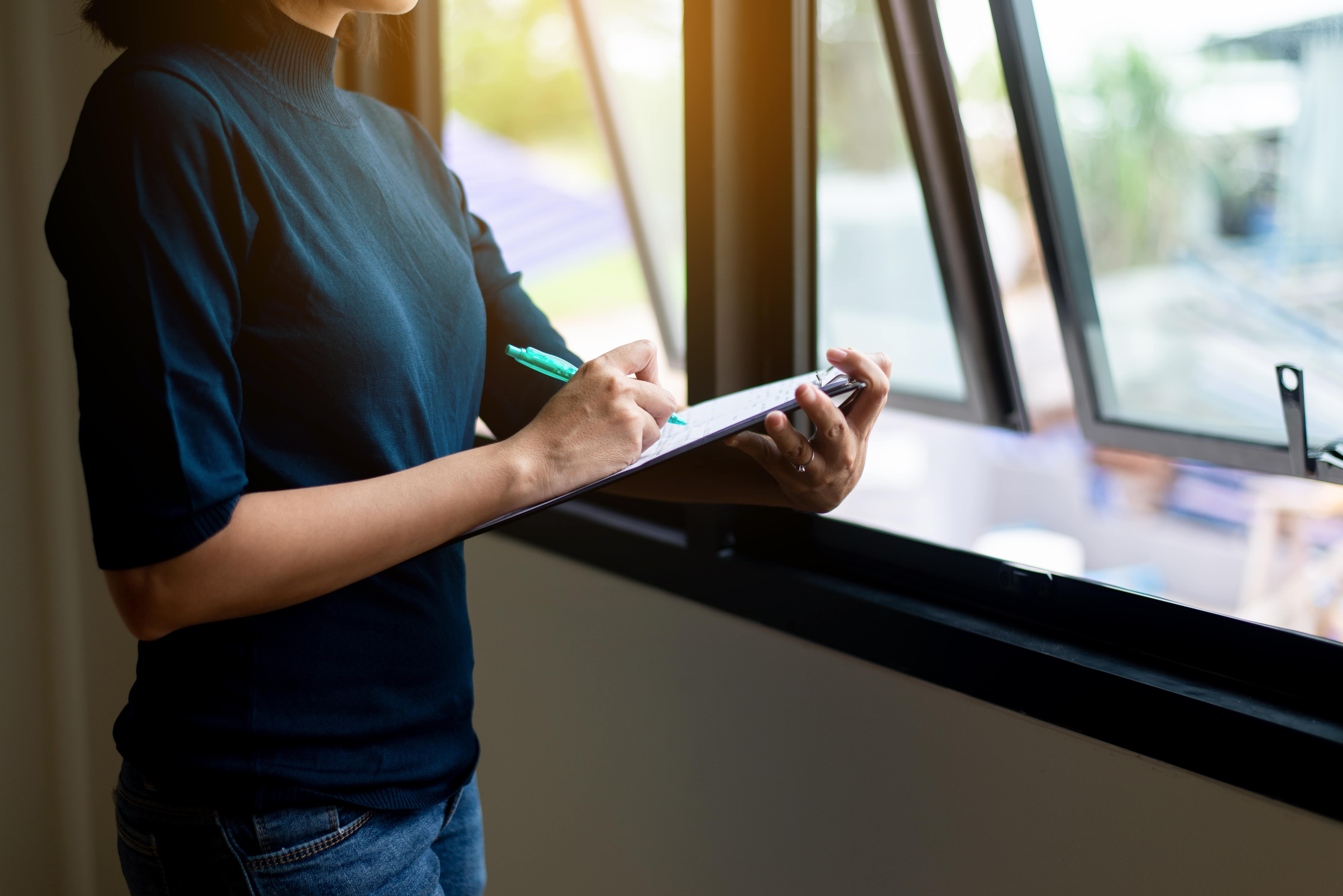 A person holding a clipboard while inspecting a property window, showcasing the role of property inspections in successful property management.