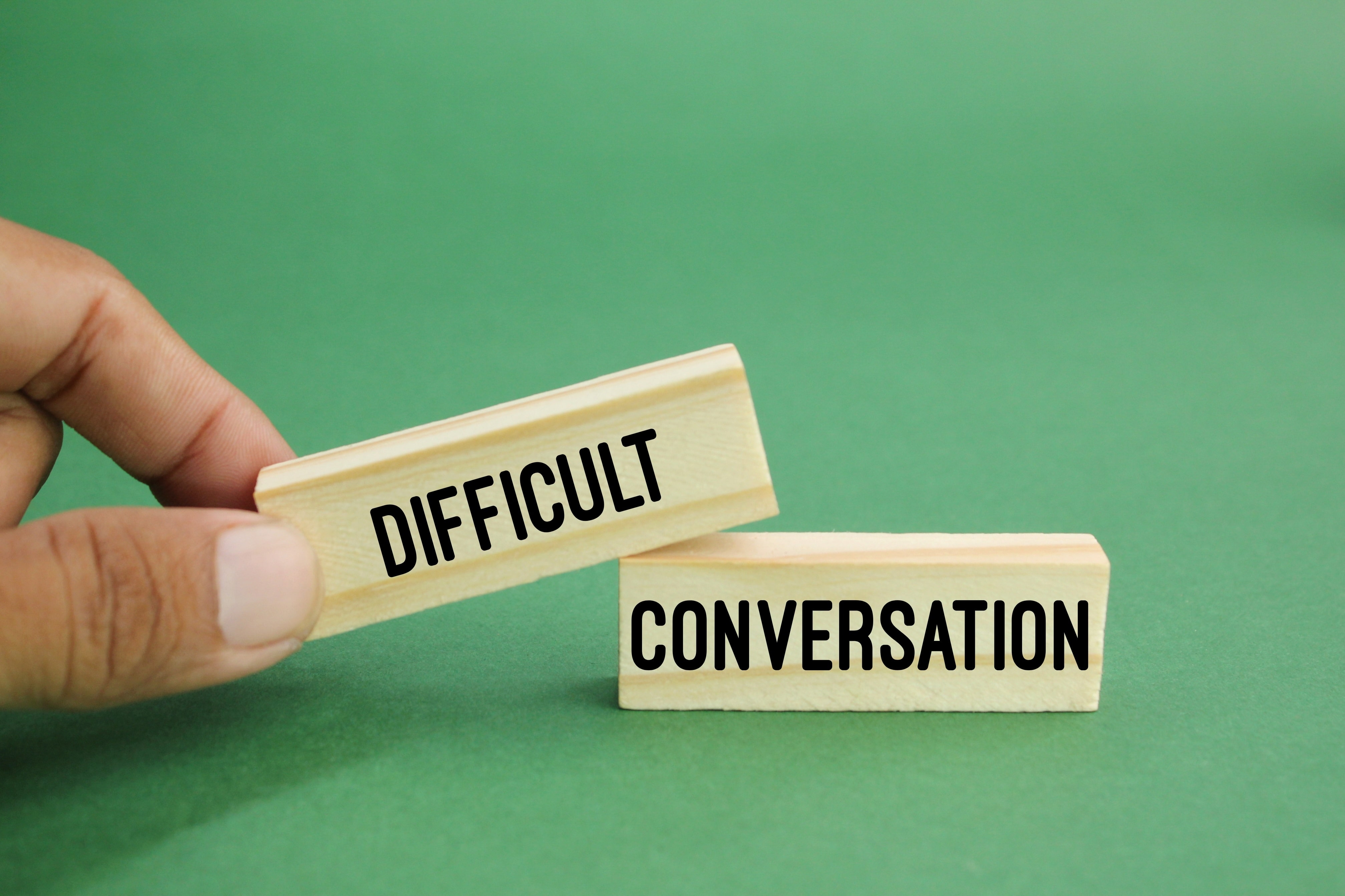 Two wooden blocks labeled ‘Difficult’ and ‘Conversation,’ signifying the importance of effective communication and conflict resolution skills for property managers.