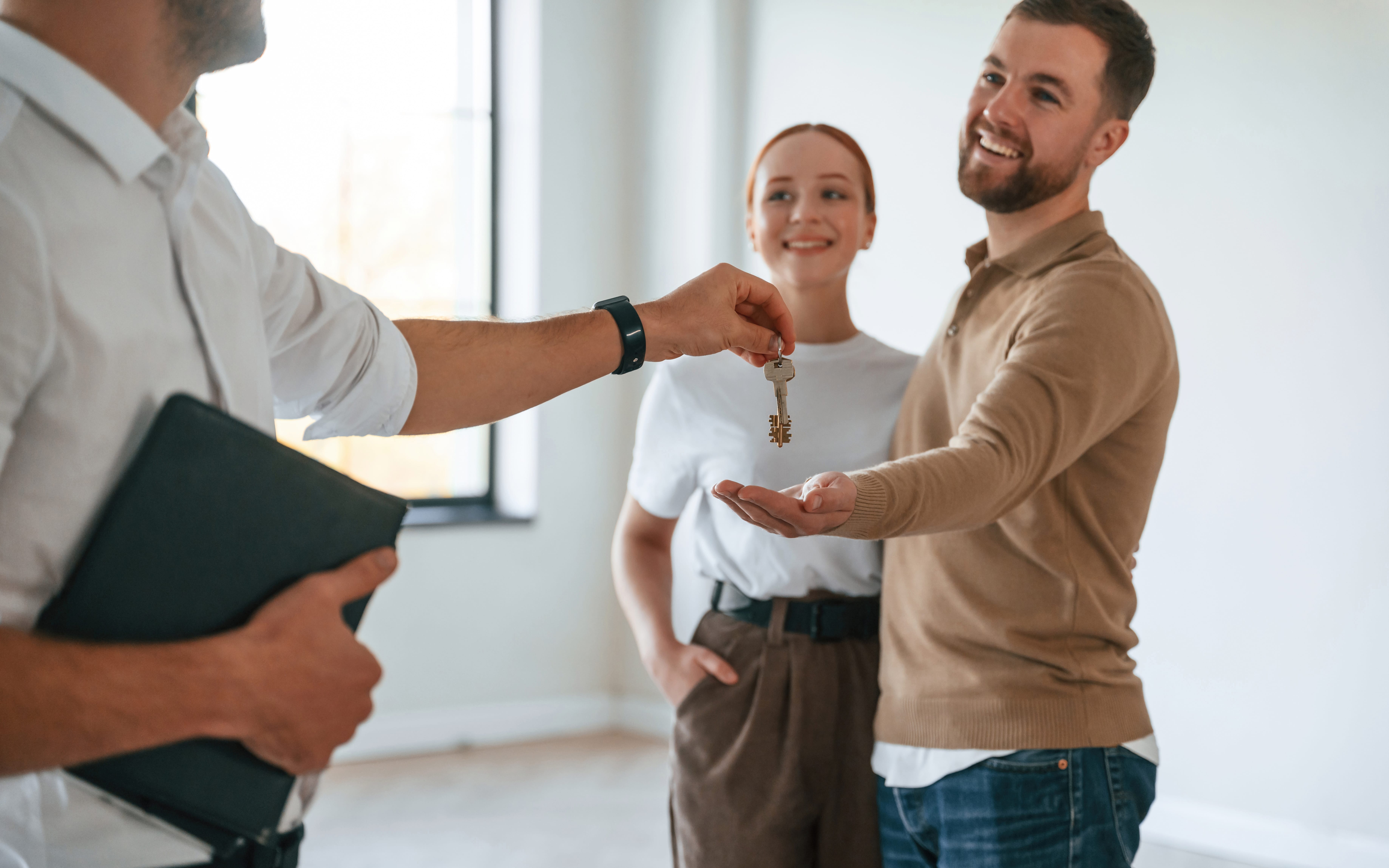 A real estate professional handing over keys to a smiling couple, symbolizing leasing and tenant relations—essential skills for becoming a property manager.