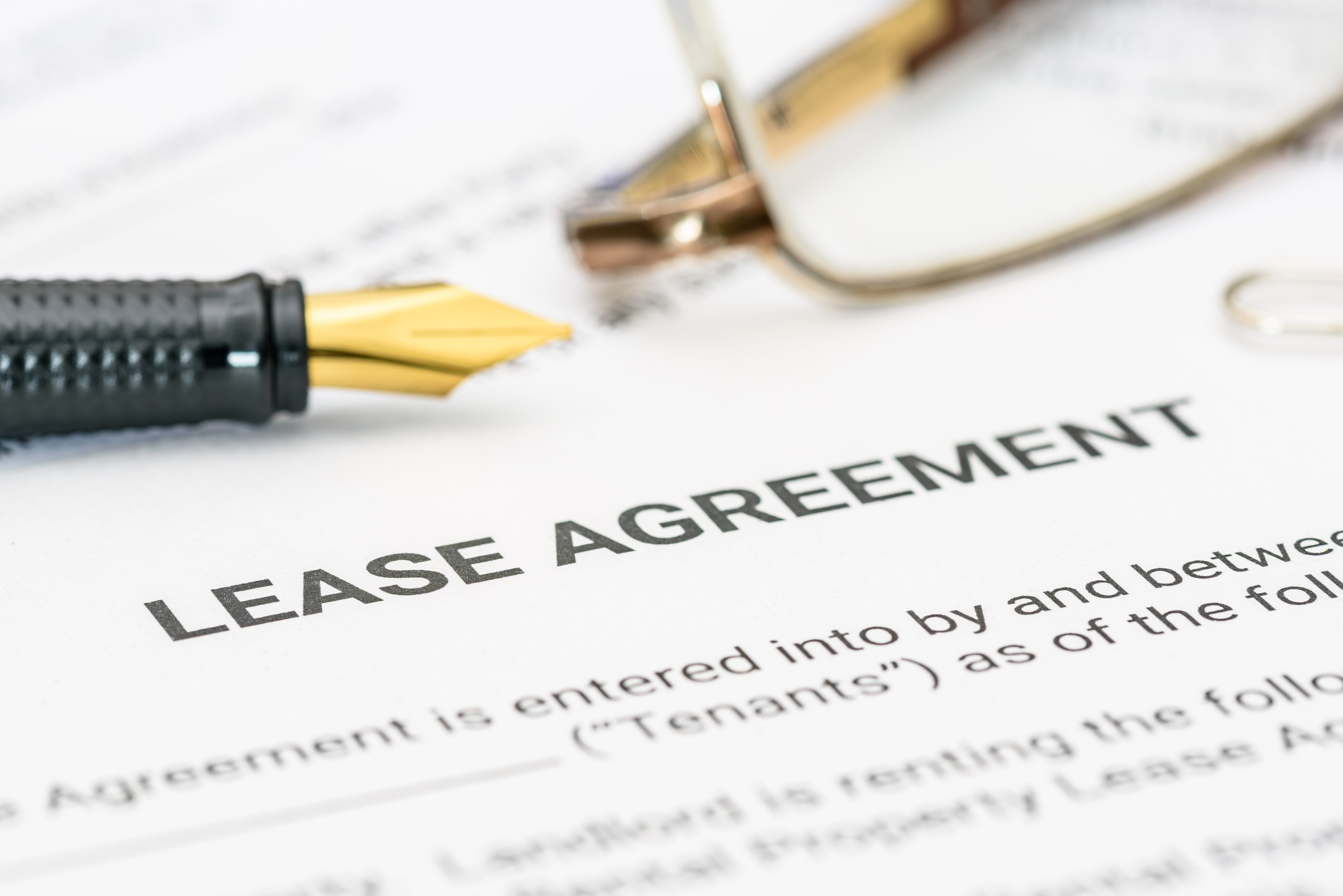 Close-up of a lease agreement document with a fountain pen and reading glasses, representing the process of signing a rental contract.