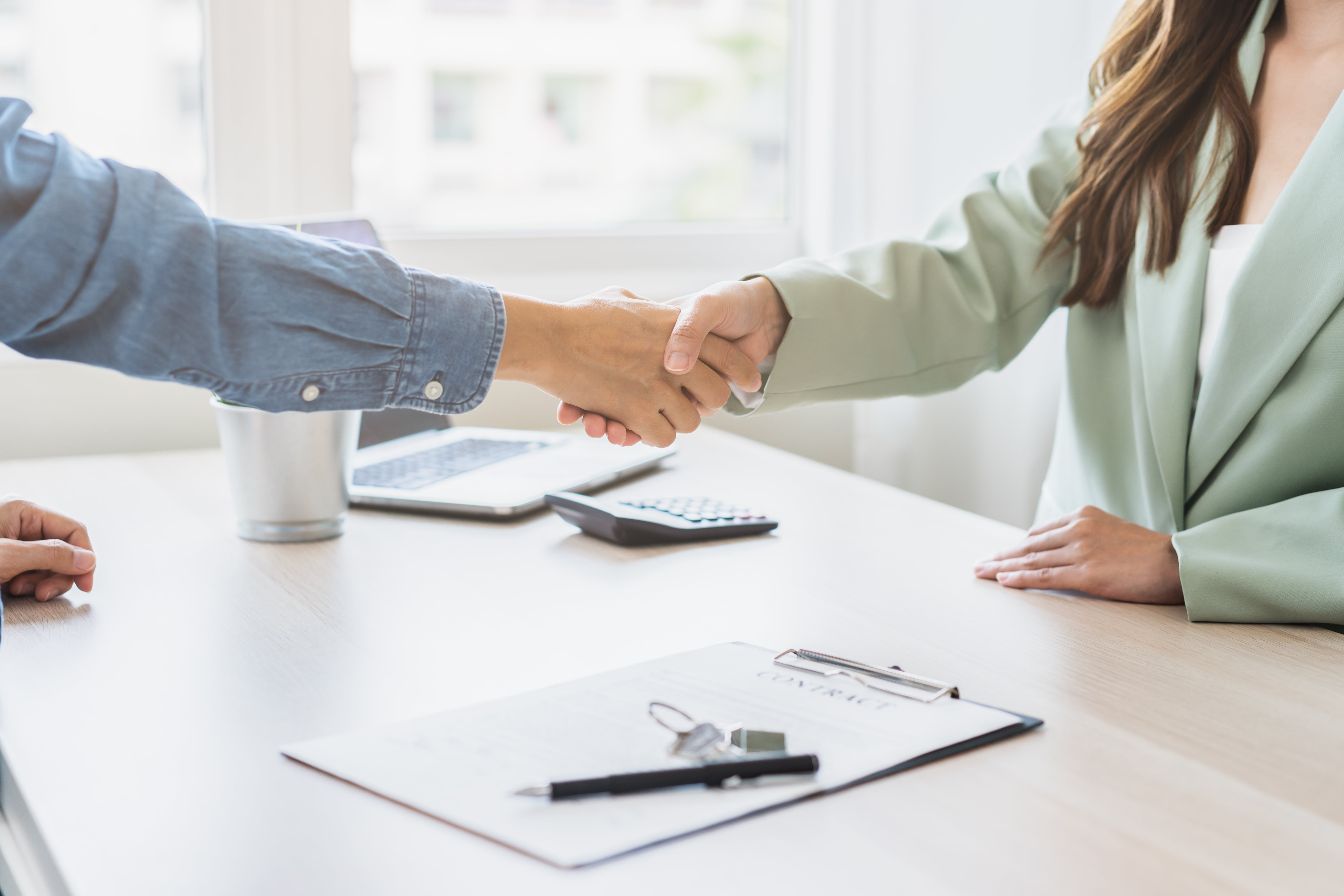 Two people shaking hands over a rental contract with keys on the table, representing a successful lease negotiation and renewal.