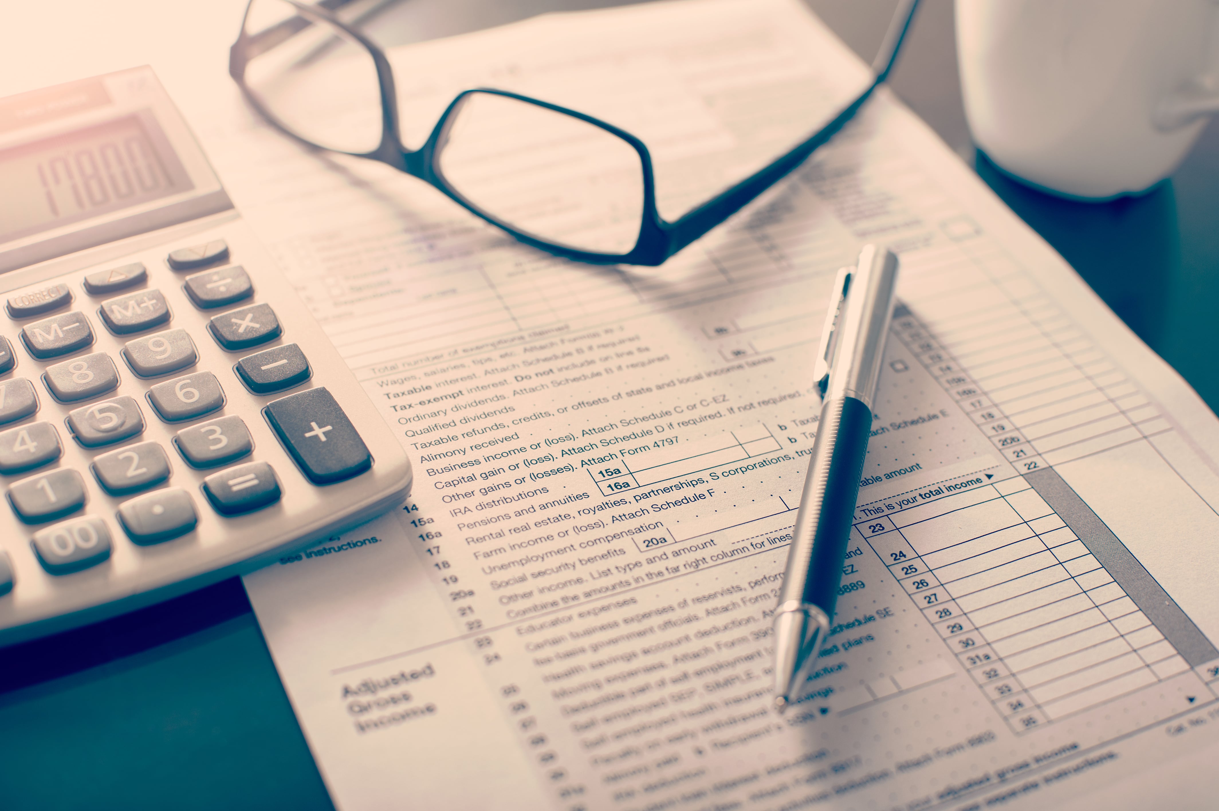 A close-up of a calculator, pen, and glasses resting on tax forms, representing financial and tax considerations for businesses.