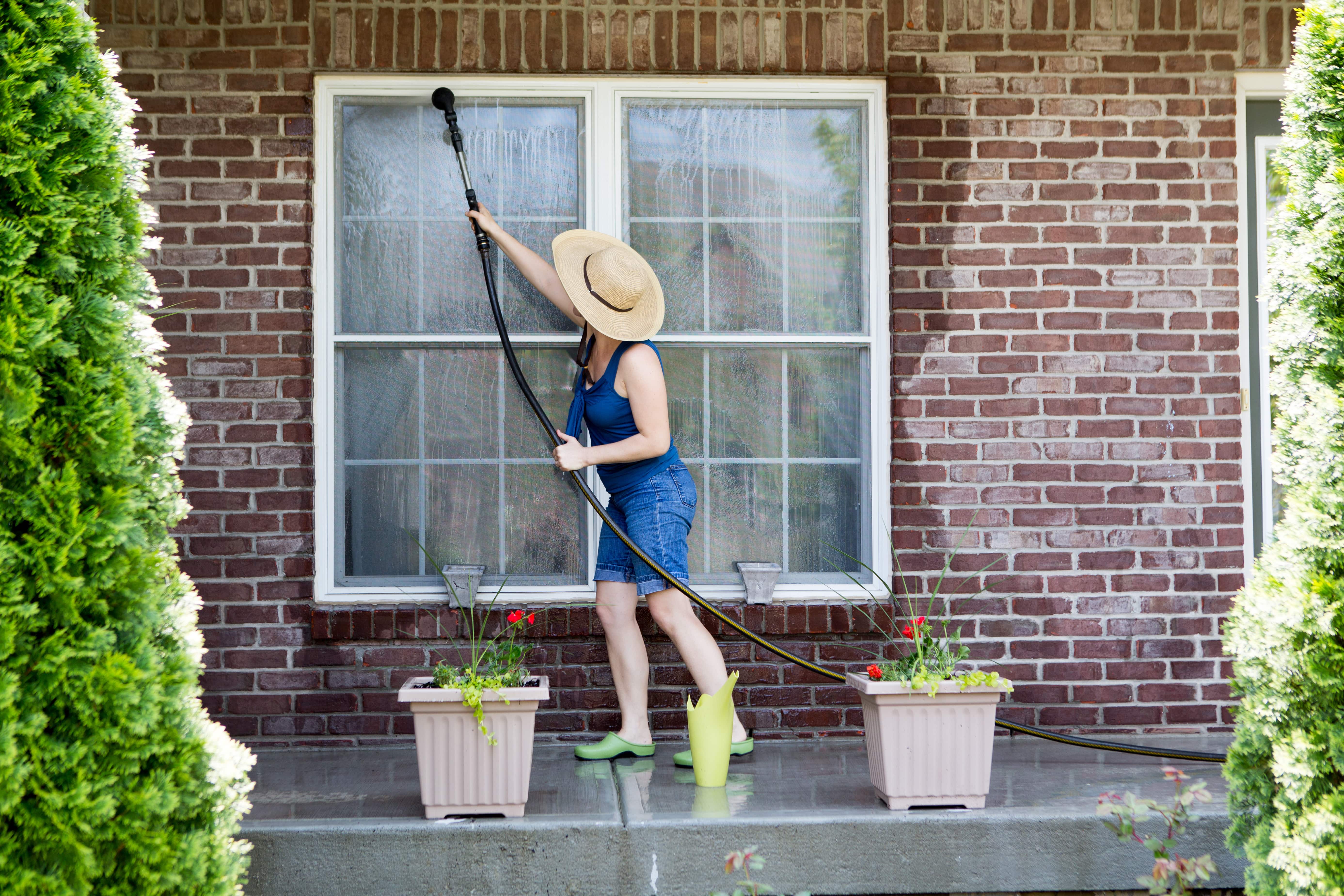 Woman washing the exterior windows of a brick house as part of her spring cleaning routine.