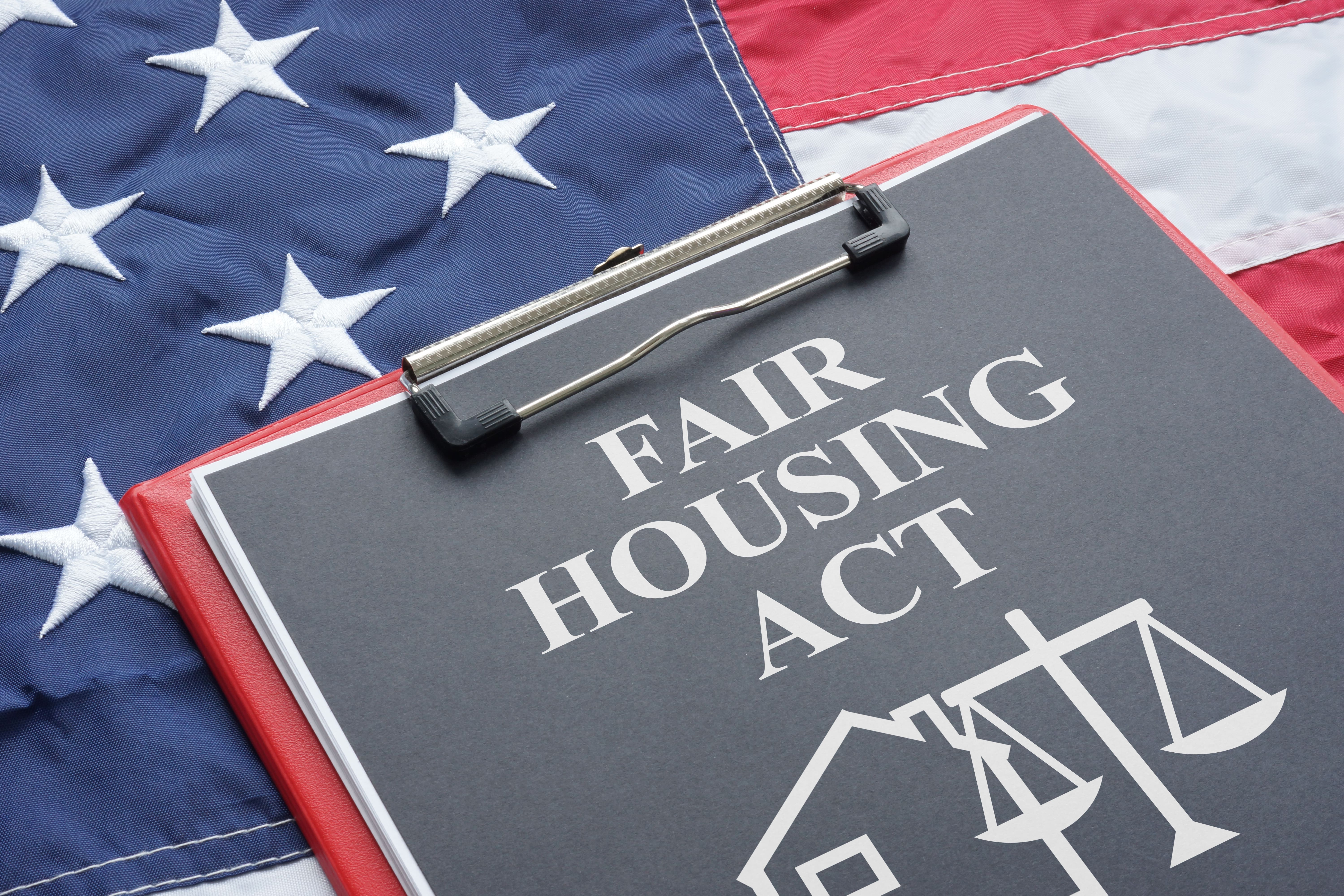 Fair Housing Act document on a clipboard, placed over an American flag, symbolizing housing rights and legal protections.