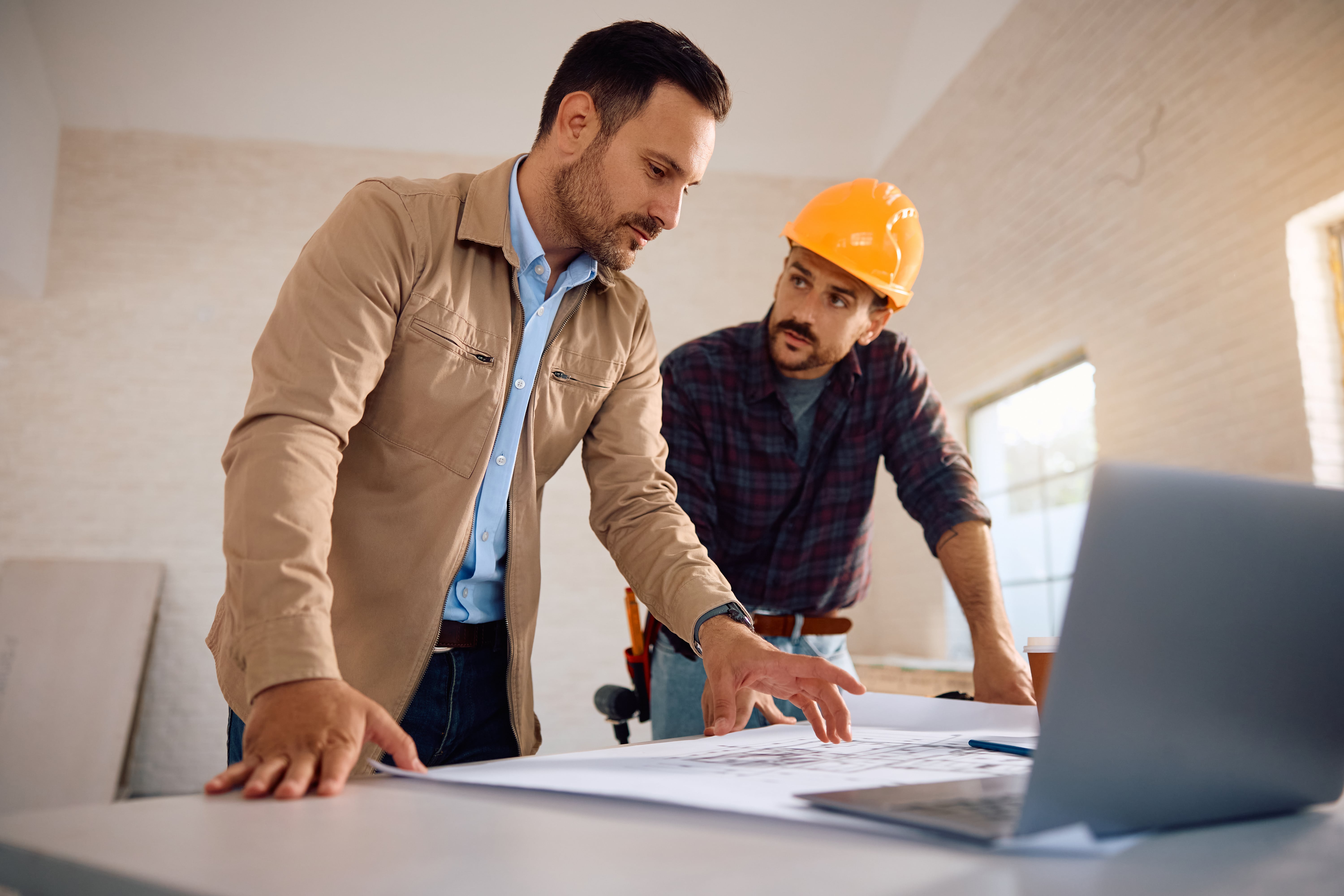 A landlord and a contractor in a hard hat, reviewing blueprints, symbolizing property maintenance and landlord responsibilities.