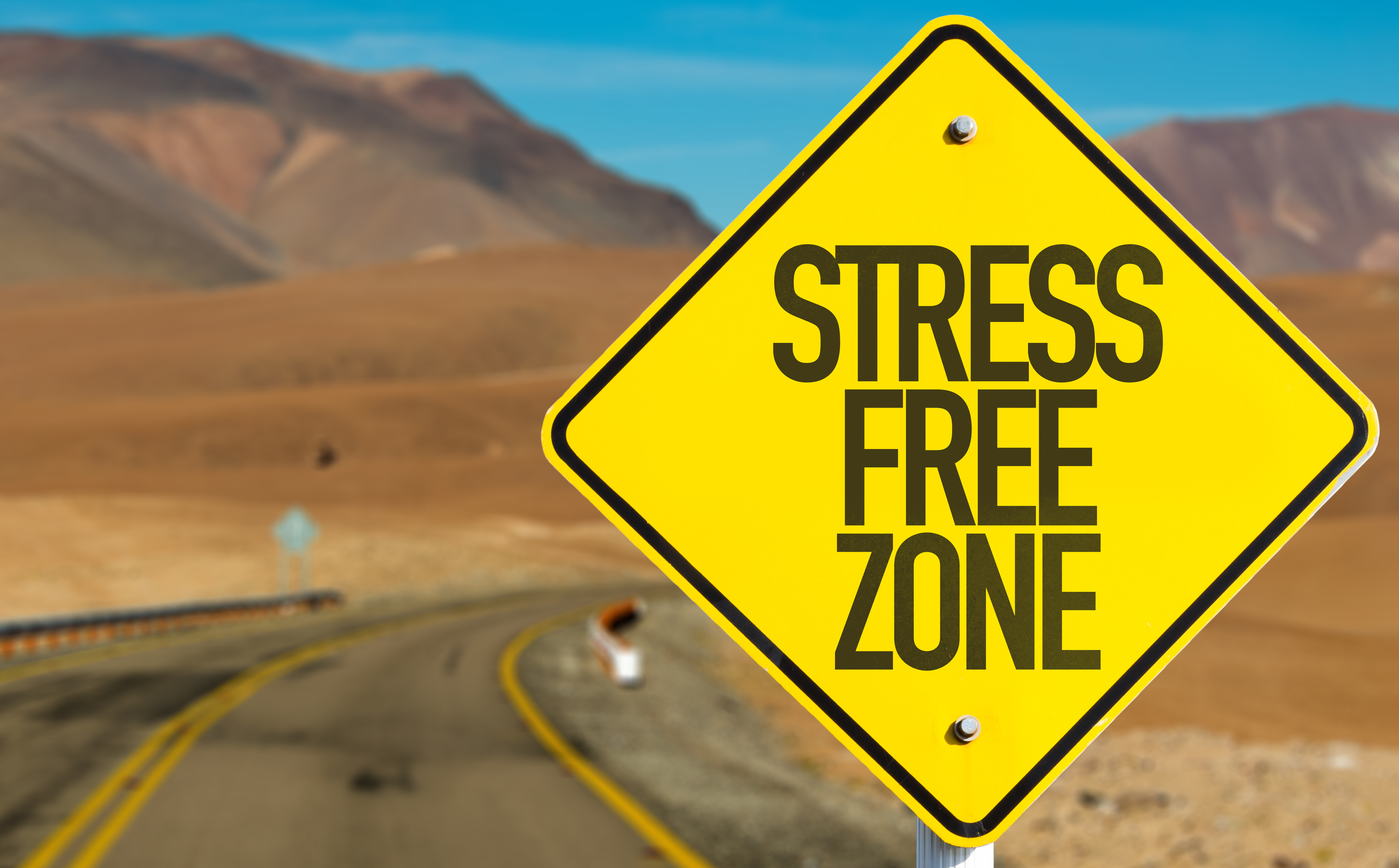 A yellow road sign with the words ‘STRESS FREE ZONE’ on an empty desert highway, symbolizing relaxation, peace, and freedom from stress.