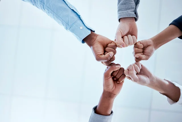 A diverse team forming a unity circle with their fists, symbolizing trust and teamwork at Allegiant Management Group.