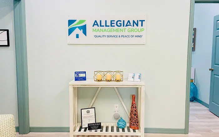 Interior office space of Allegiant Management Group featuring a decorative white console table, branded signage on the wall, and various awards and decorative items.