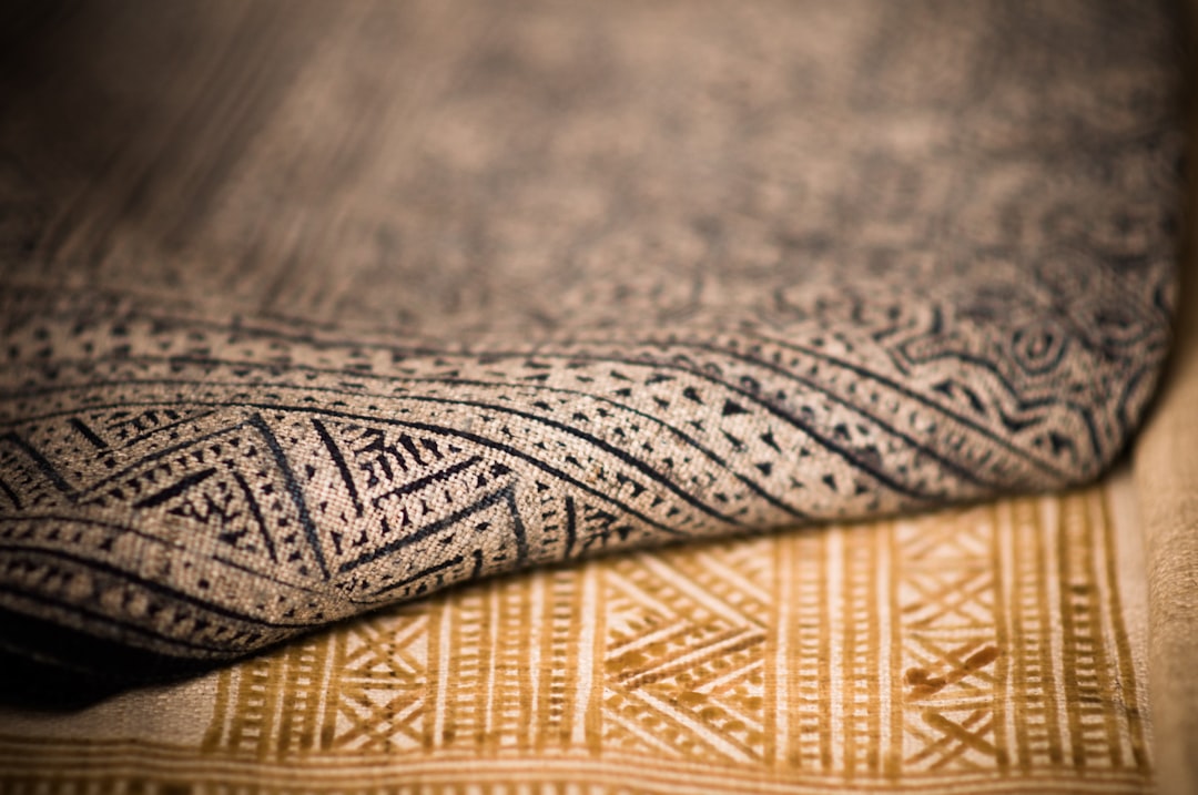 Close-up of a folded patterned carpet with intricate designs. The foreground shows a detailed view of the texture and patterns, highlighting craftsmanship.