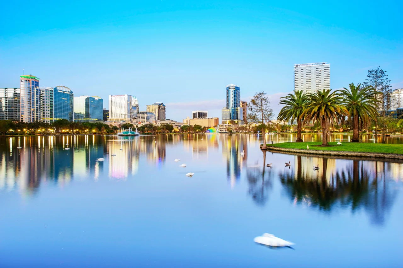 Downtown Orlando skyline reflecting on Lake Eola at dusk with palm trees and modern high-rises, highlighting Central Florida real estate market.