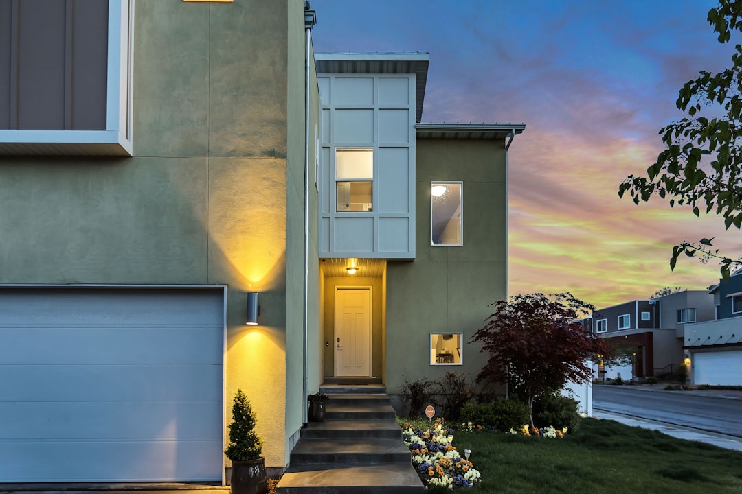 A modern house with a well-lit exterior and a landscaped front yard during sunset.