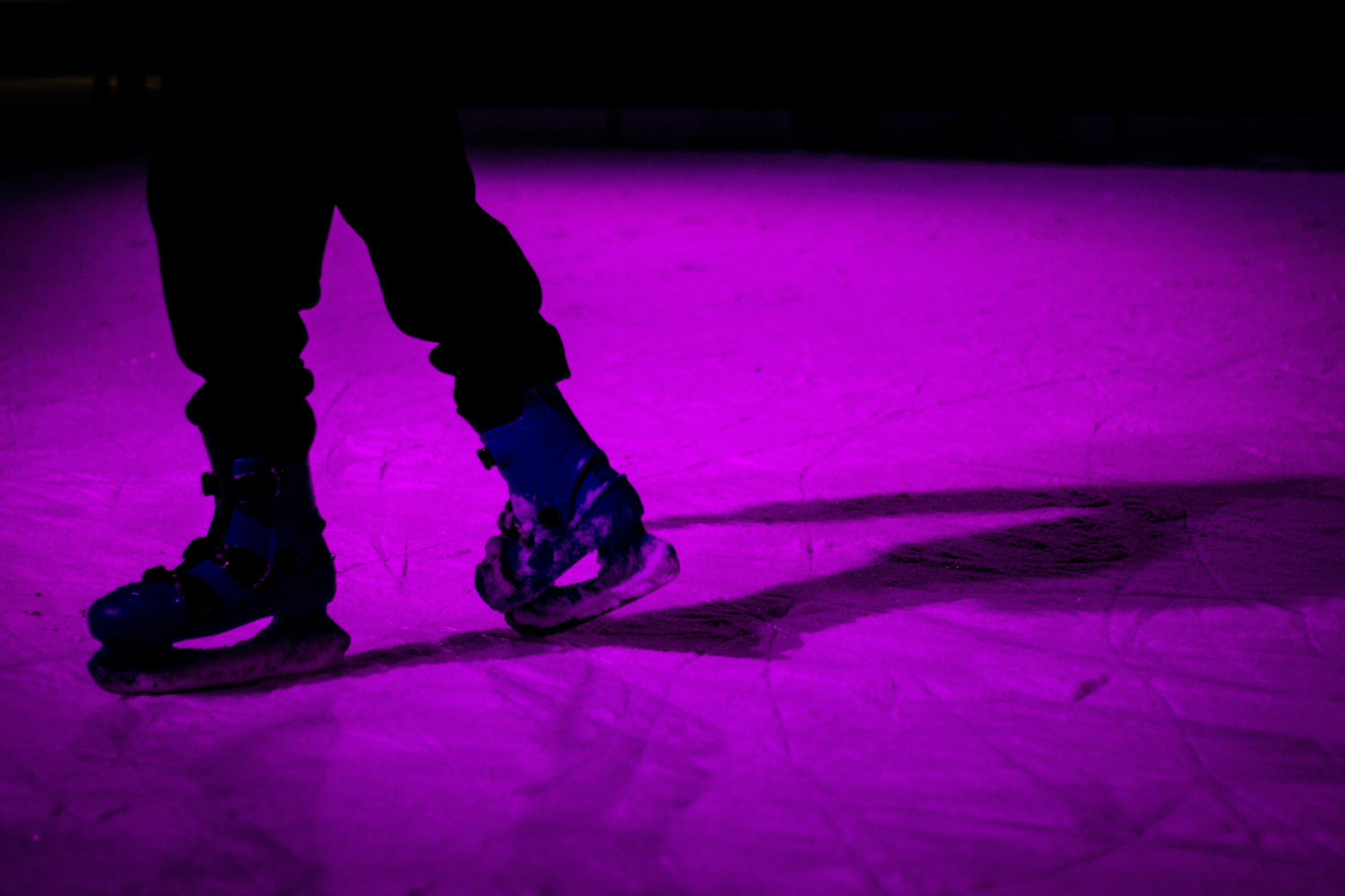 Close-up of an ice skater wearing blue skates on a rink bathed in vibrant purple light. Photo by Vasilios Muselimis on Unsplash